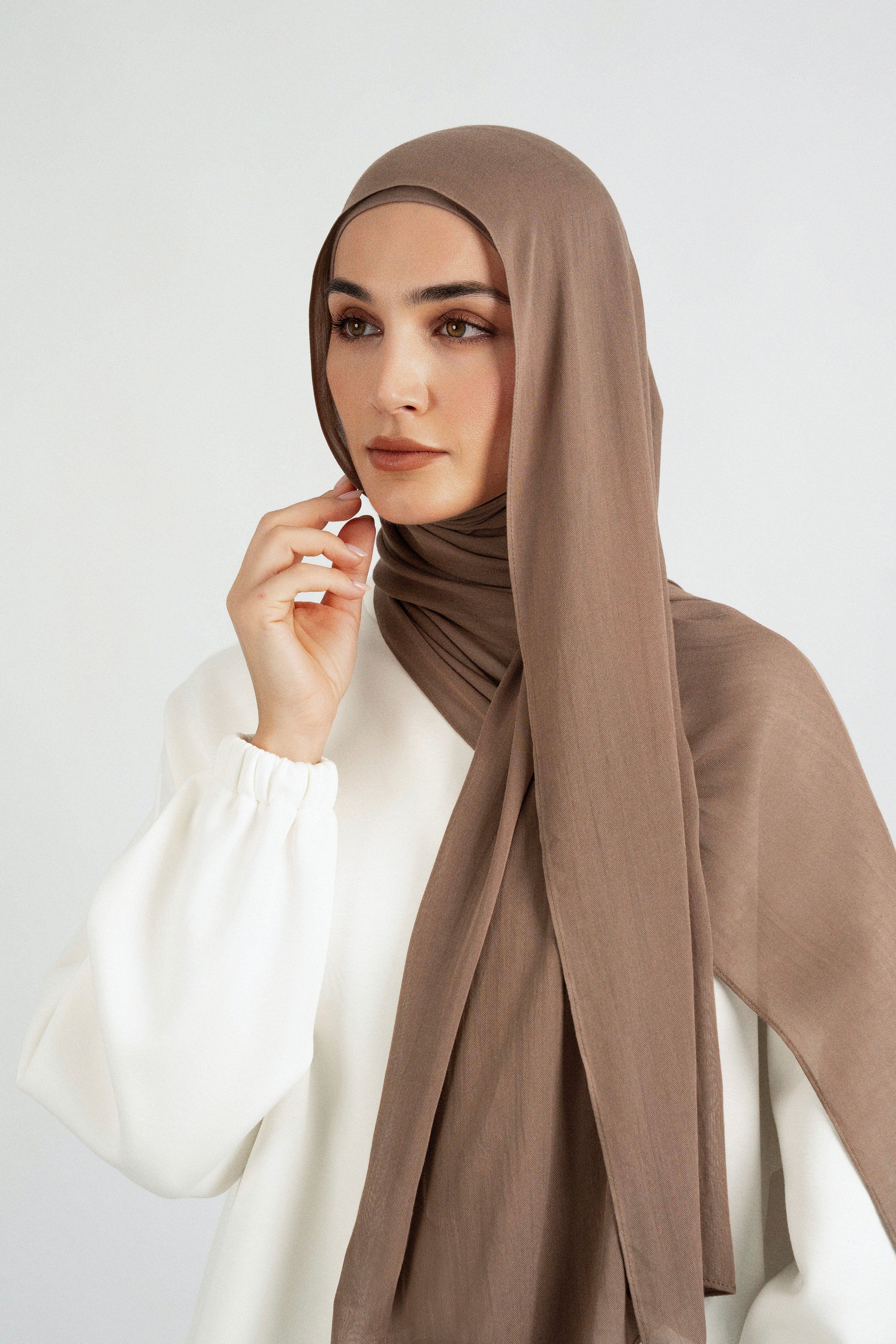 A model is wearing a Matching Butter Modal Hijab Set and touching her face. Colour: Walnut.