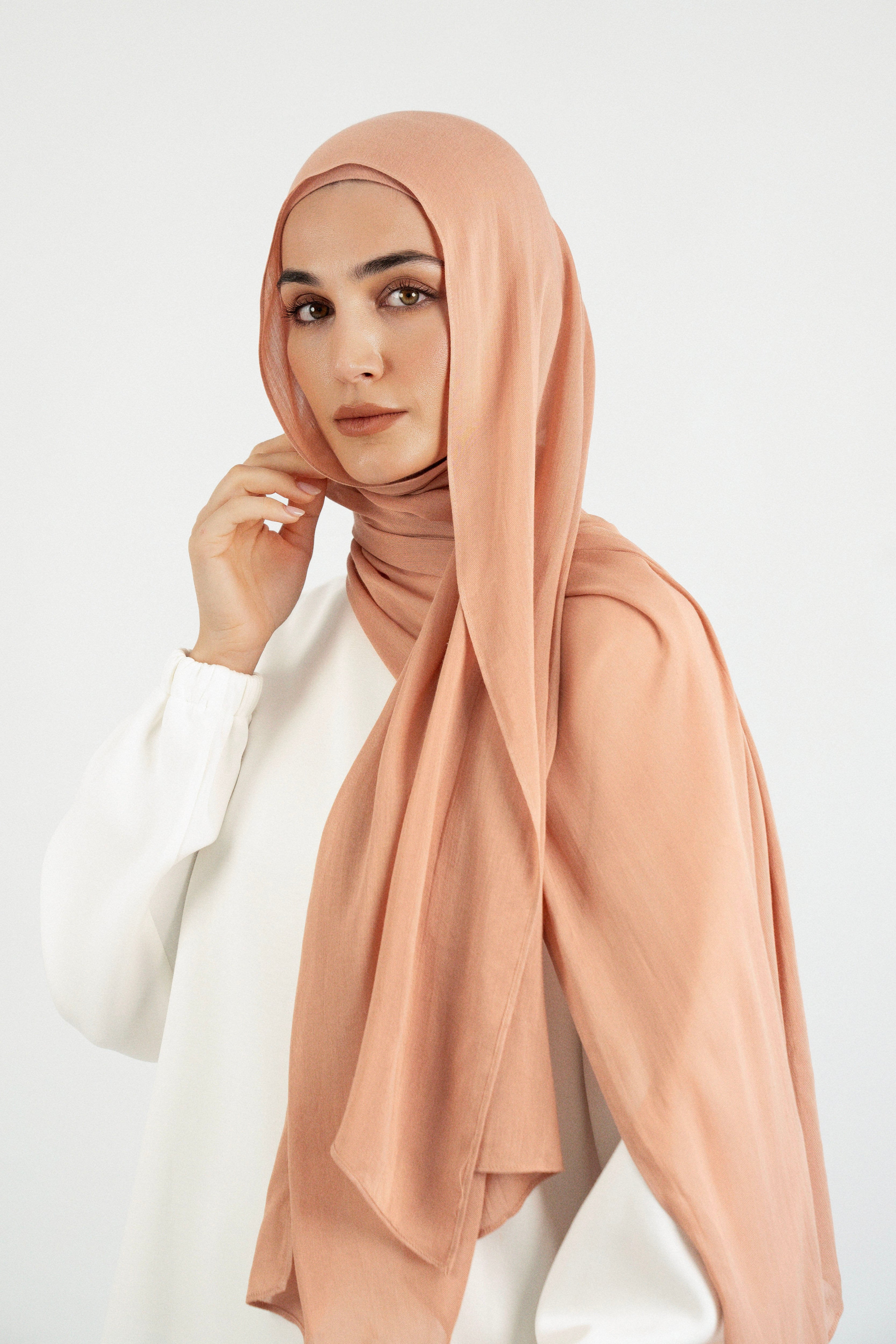 Colour: Clay. A model is wearing a Matching Butter Modal Hijab Set and touching her face.