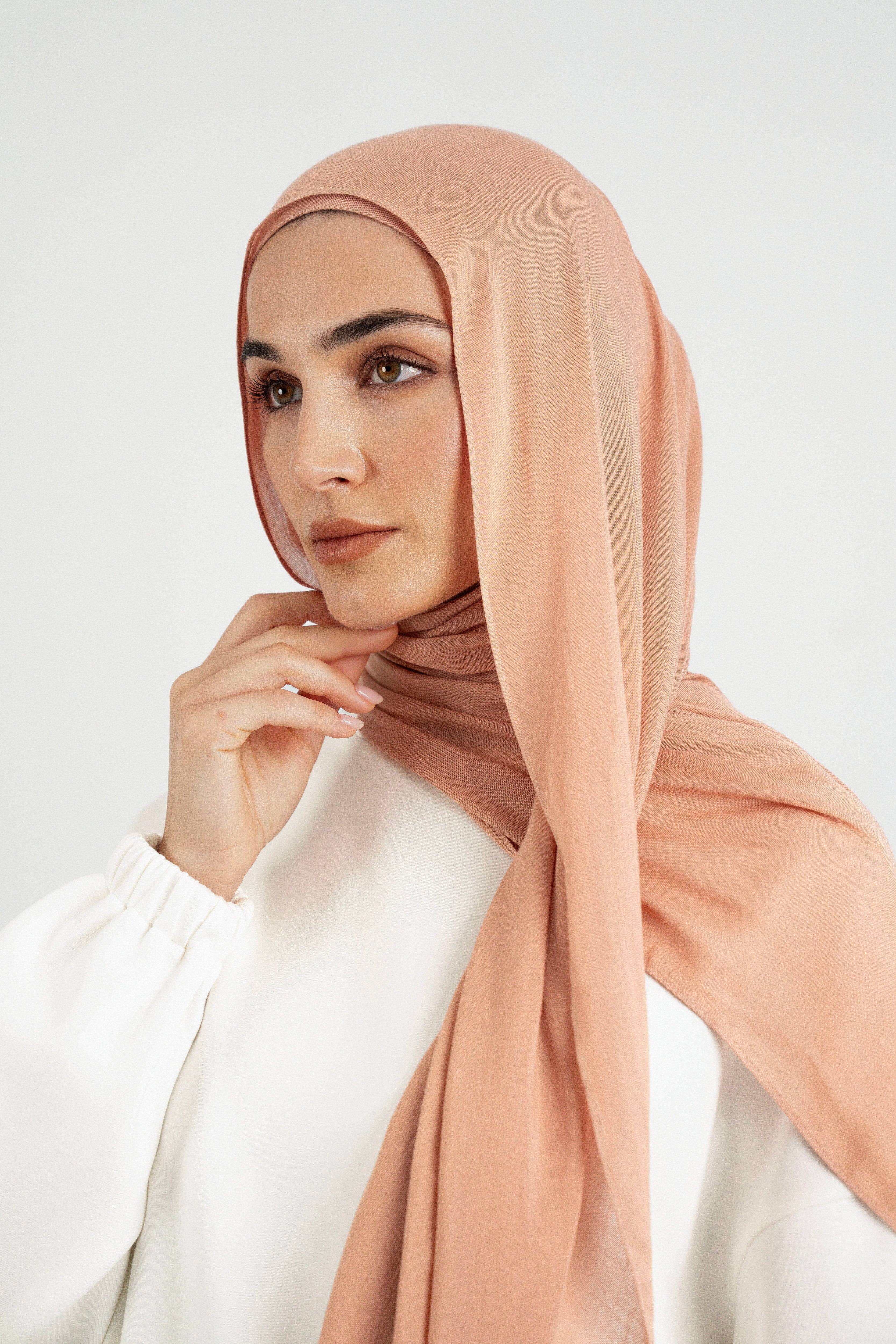 Colour: Clay. A close up of girl wearing a Matching Butter Modal Hijab Set and touching her face.