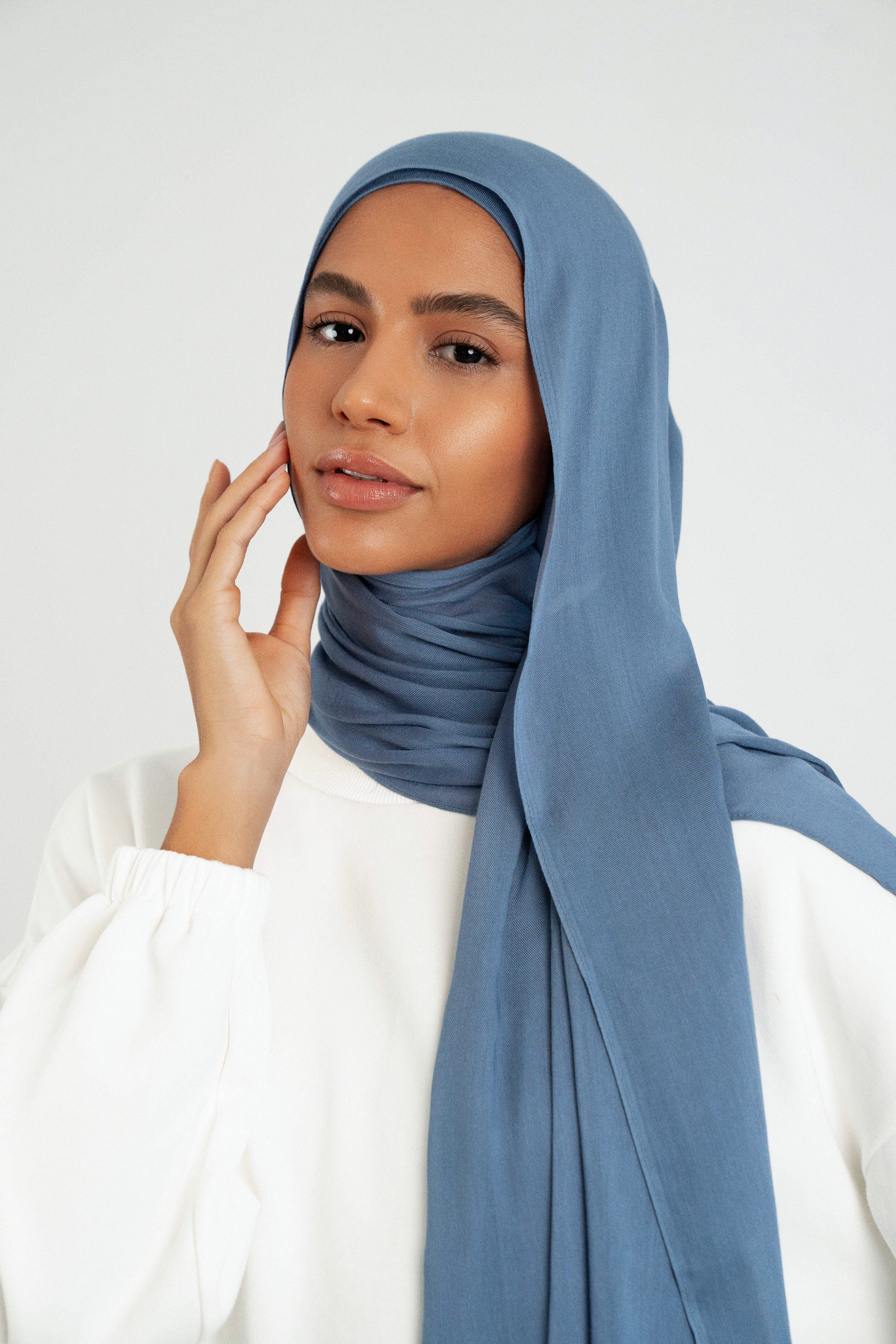 Colour: Denim. A close up of girl wearing a Matching Butter Modal Hijab Set and touching her face.
