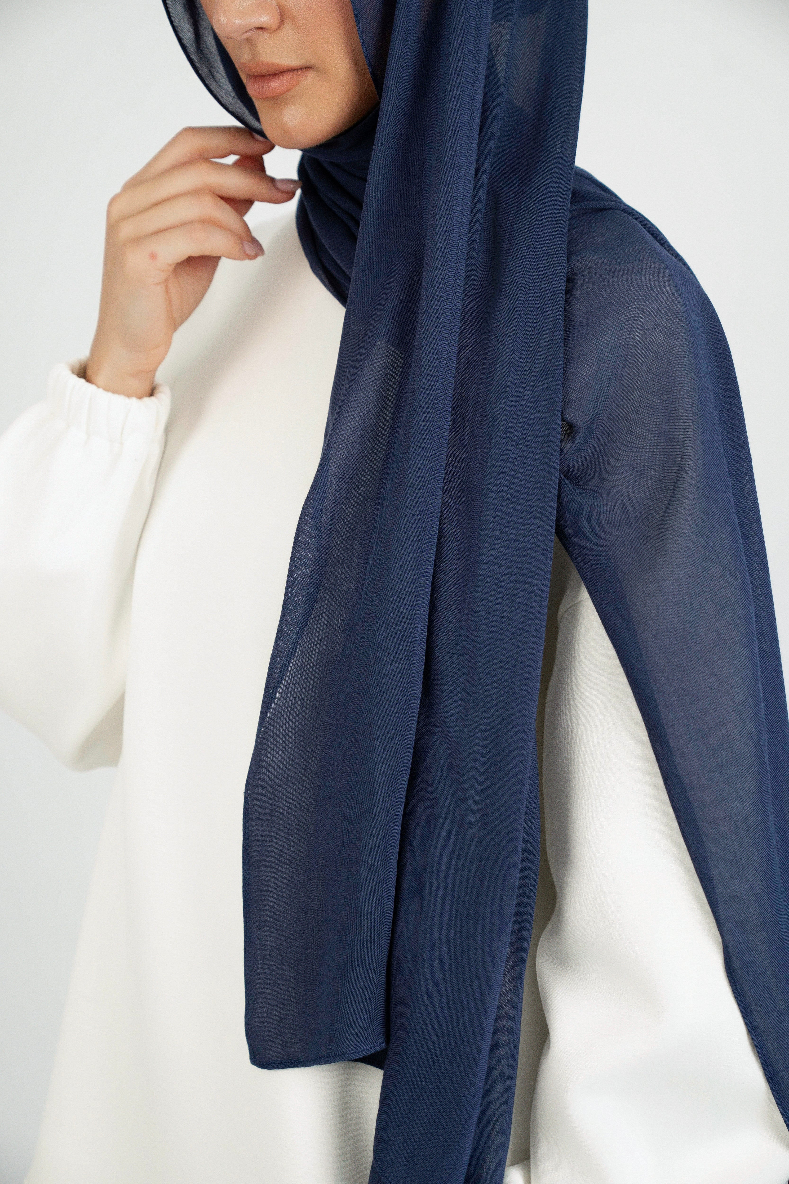 Colour: Navy. A model is wearing a Matching Butter Modal Hijab Set and touching her face.