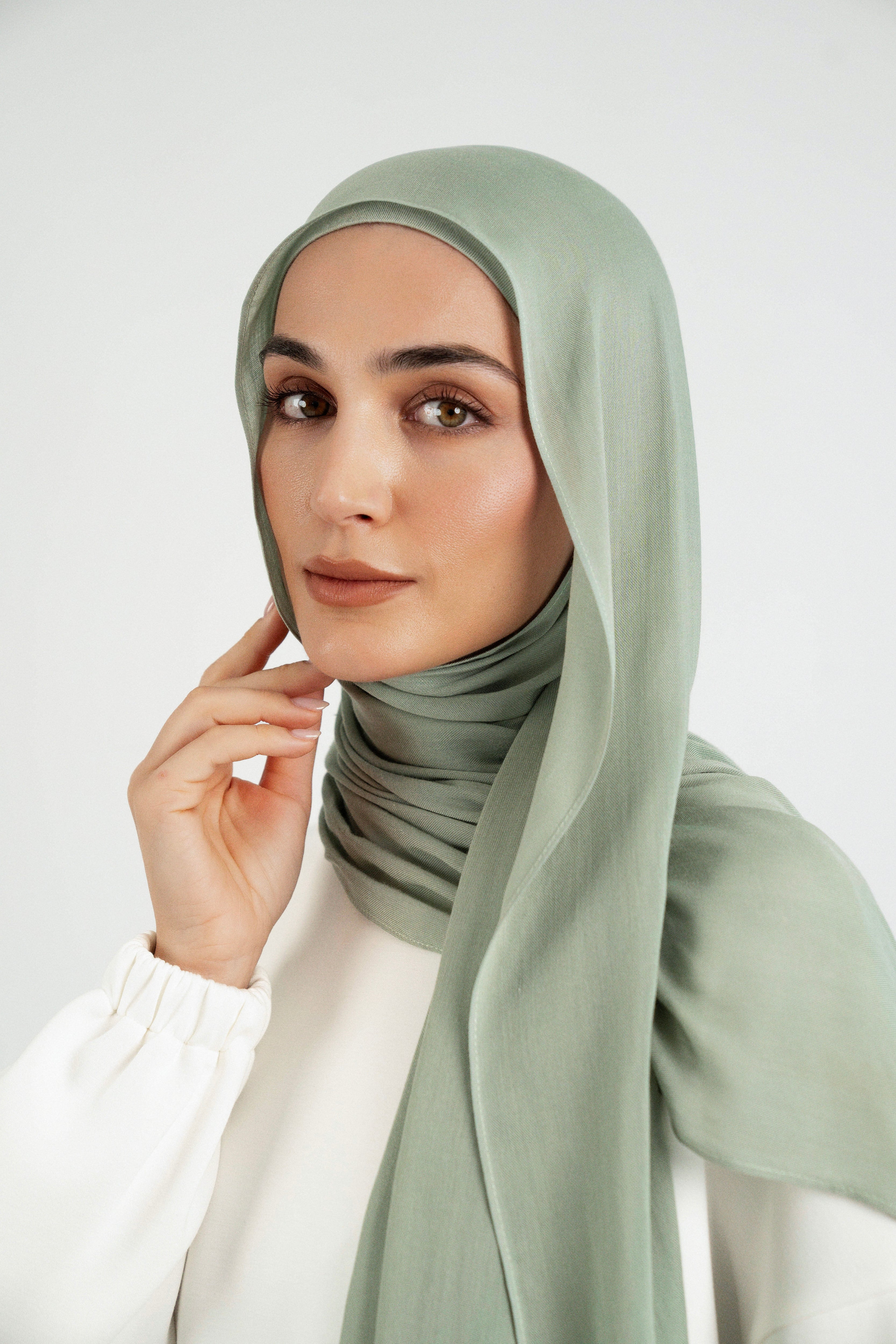 Colour: Sage. A close up of girl wearing a Matching Butter Modal Hijab Set and touching her face.