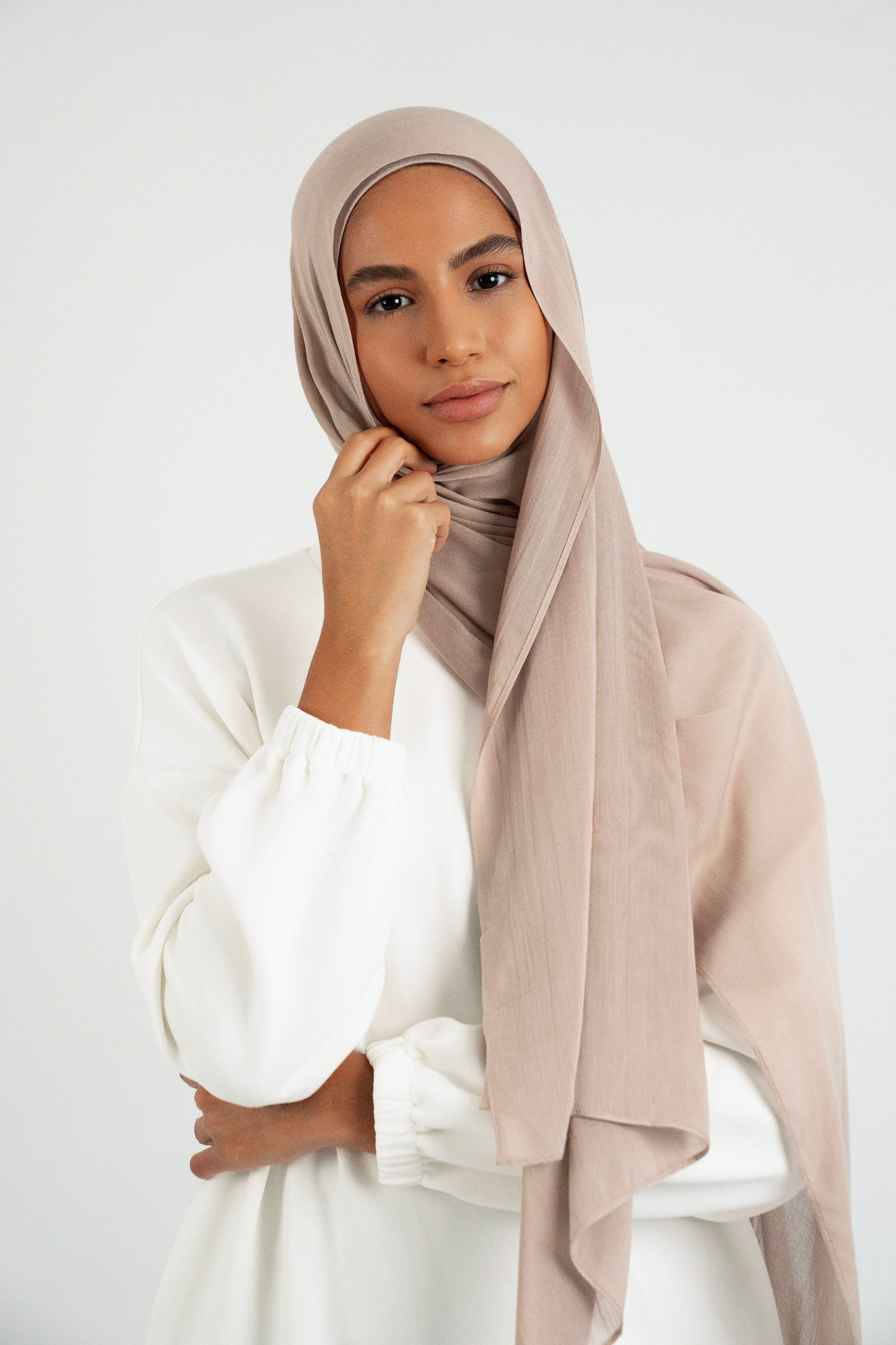 A model is wearing a Matching Butter Modal Hijab Set and touching her face. Colour: Sesame.