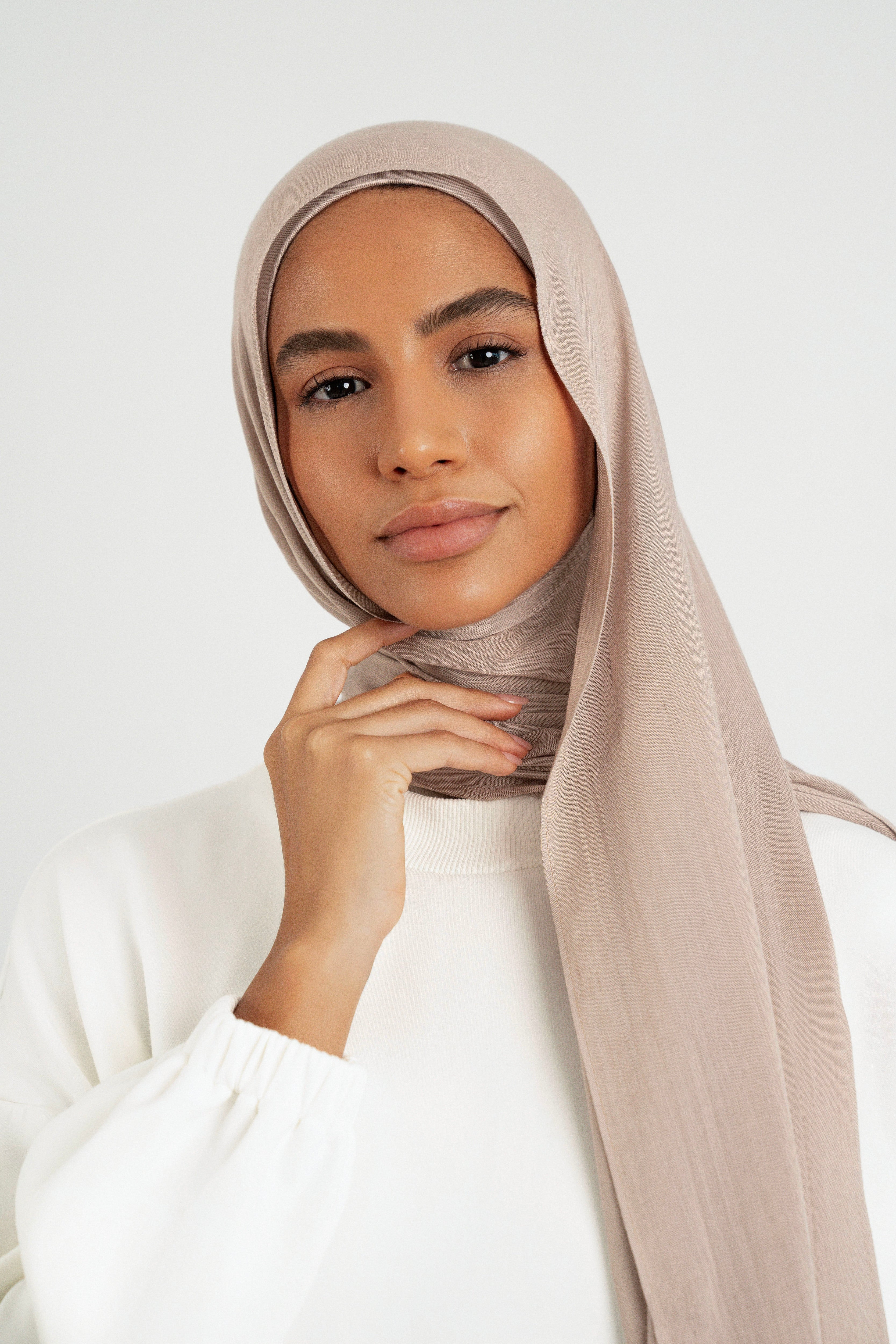 A close up of girl wearing a Matching Butter Modal Hijab Set and touching her face. Colour:  Sesame.