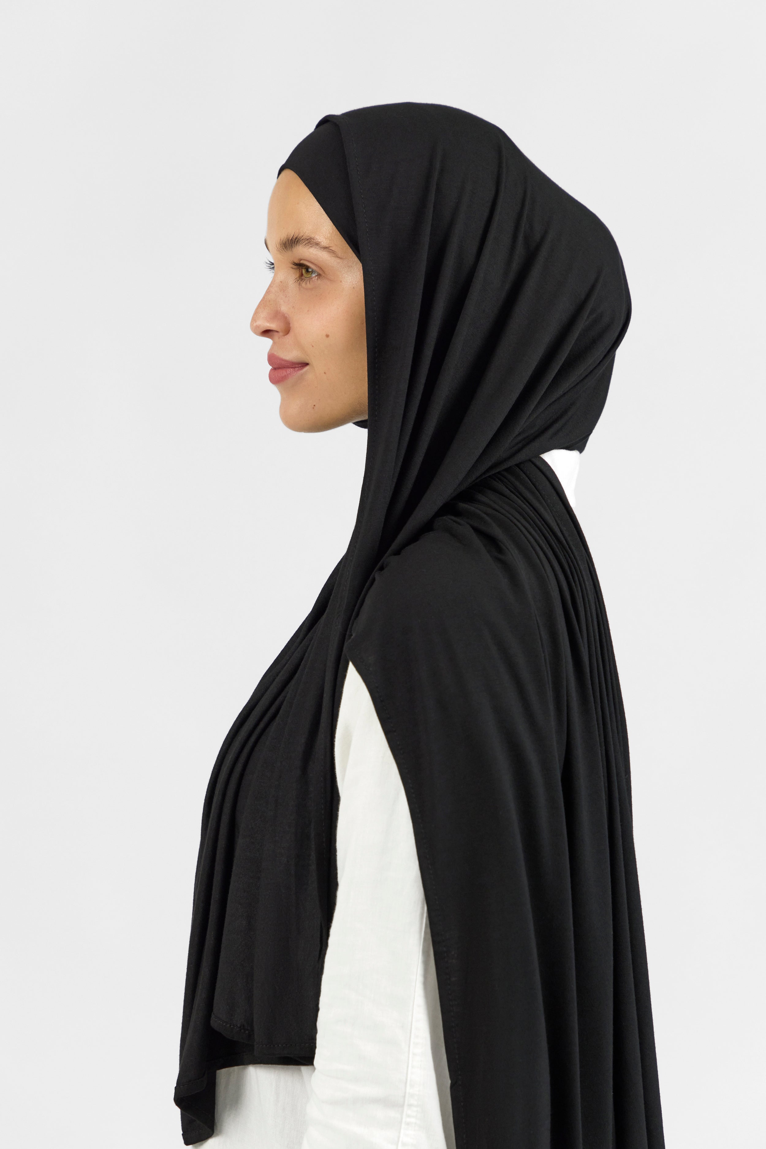 The left profile of a female model wearing one of FARES's matching jersey hijab sets. Colour description: black.