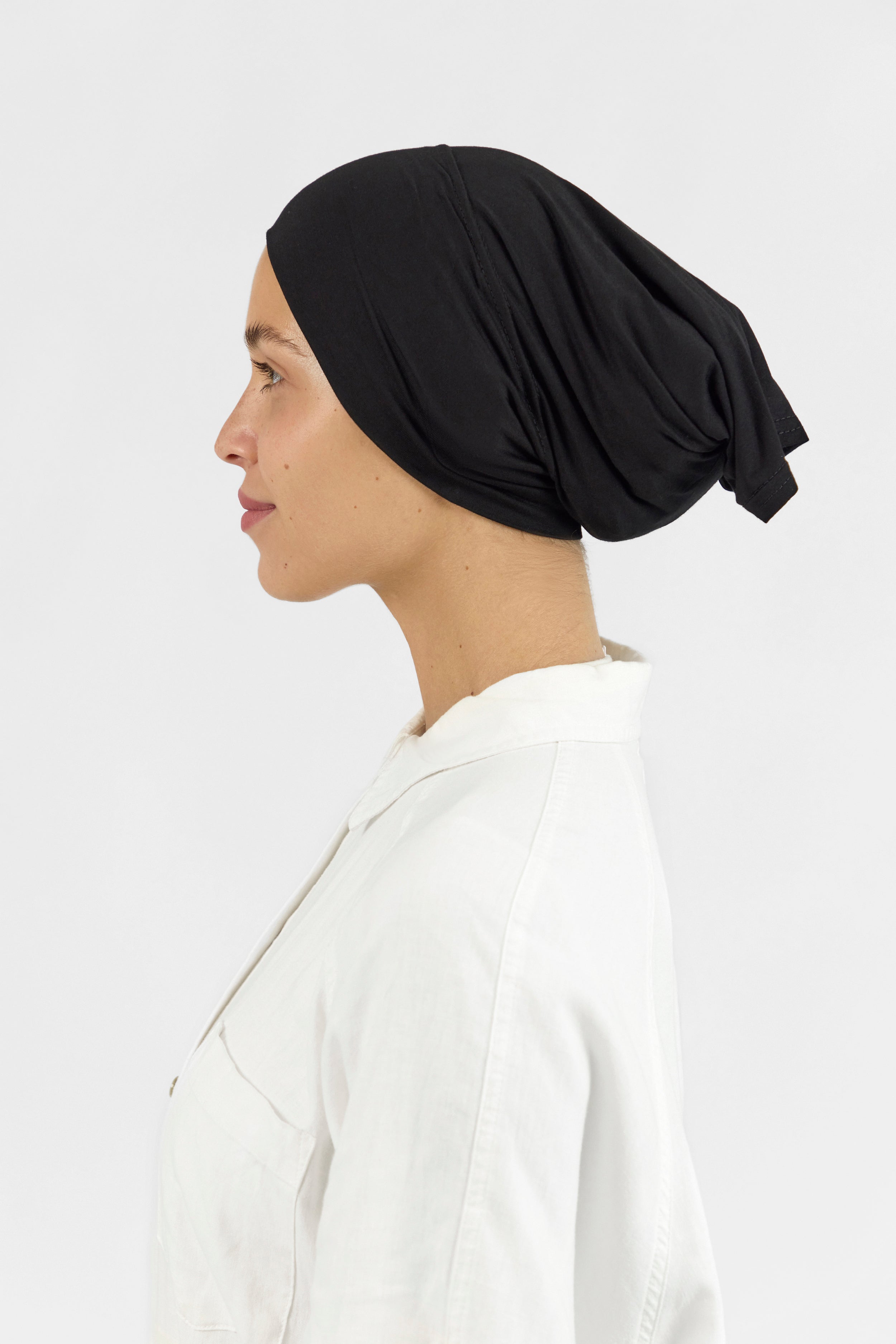 The left profile of a female model wearing a hijab undercap. Colour description: black.