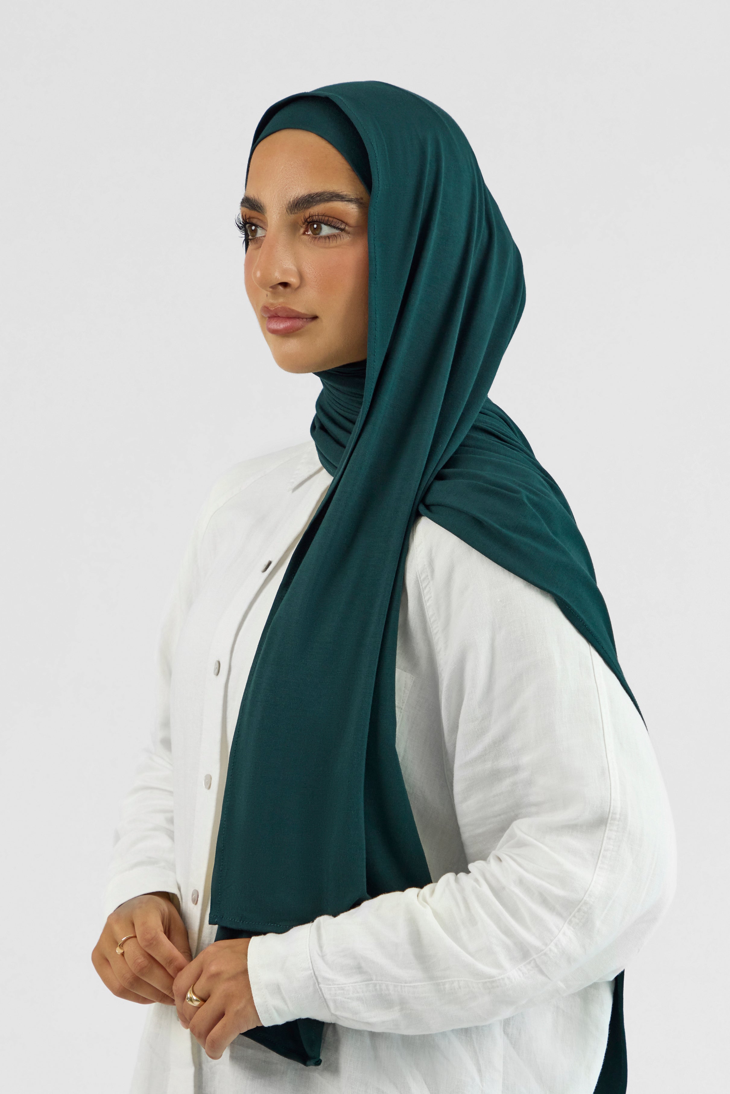 A woman wearing one of FARES's matching jersey hijab sets. The model is turned to the left. Colour description: dark teal.