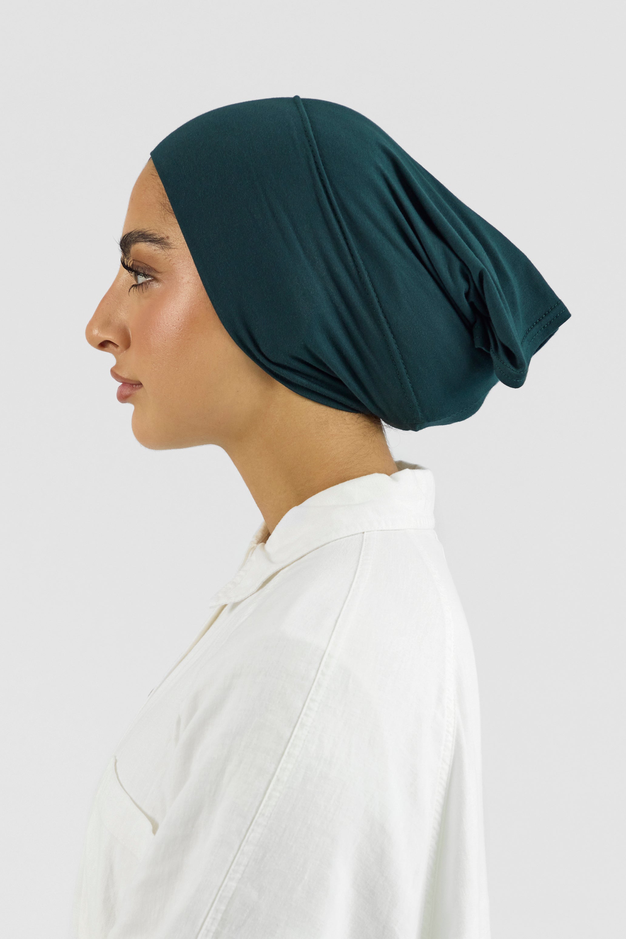 The left profile of a female model wearing a hijab undercap. Colour description: dark teal.
