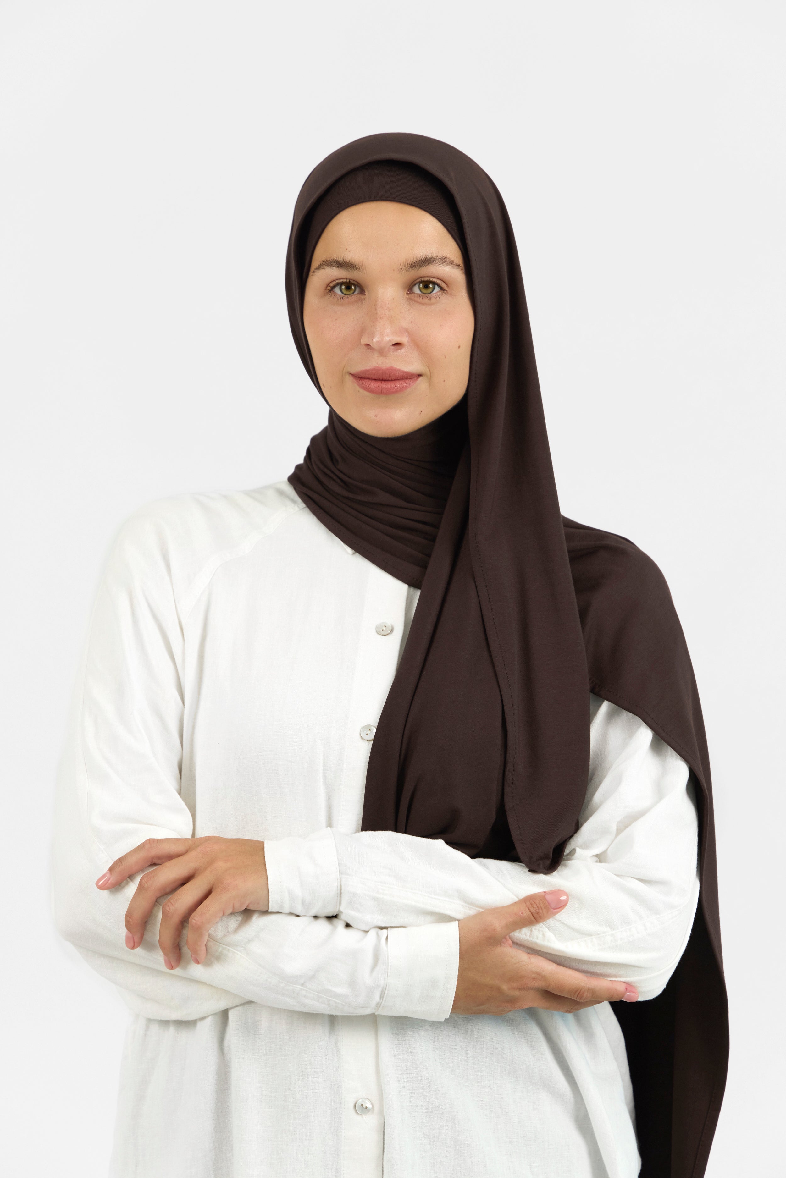 The front of a female model wearing a matching jersey hijab set. The model is crossing her arms. Colour description: dark brown.