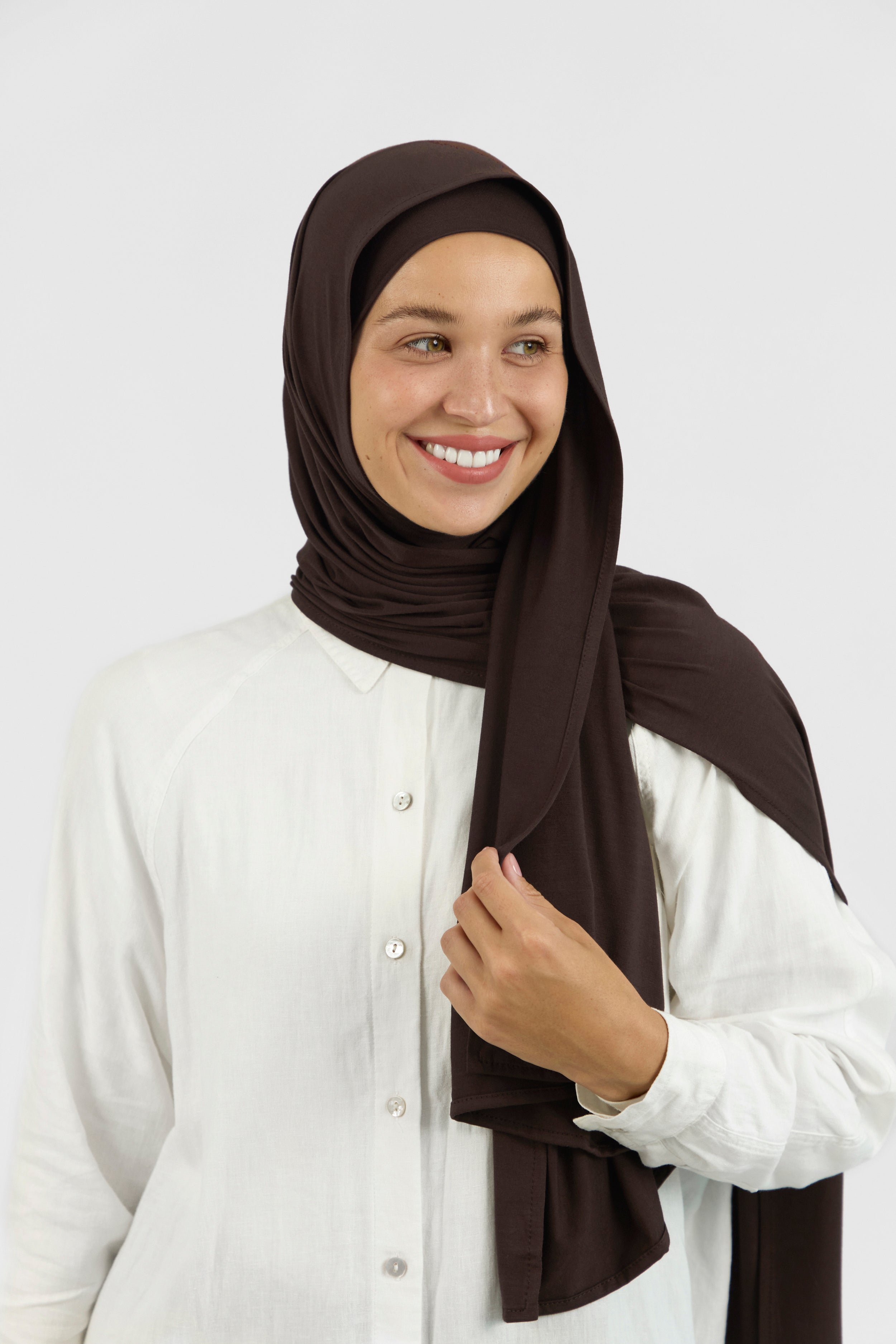 A woman wearing one of FARES's matching jersey hijab sets. The model is smiling to the right. Colour description: dark brown.