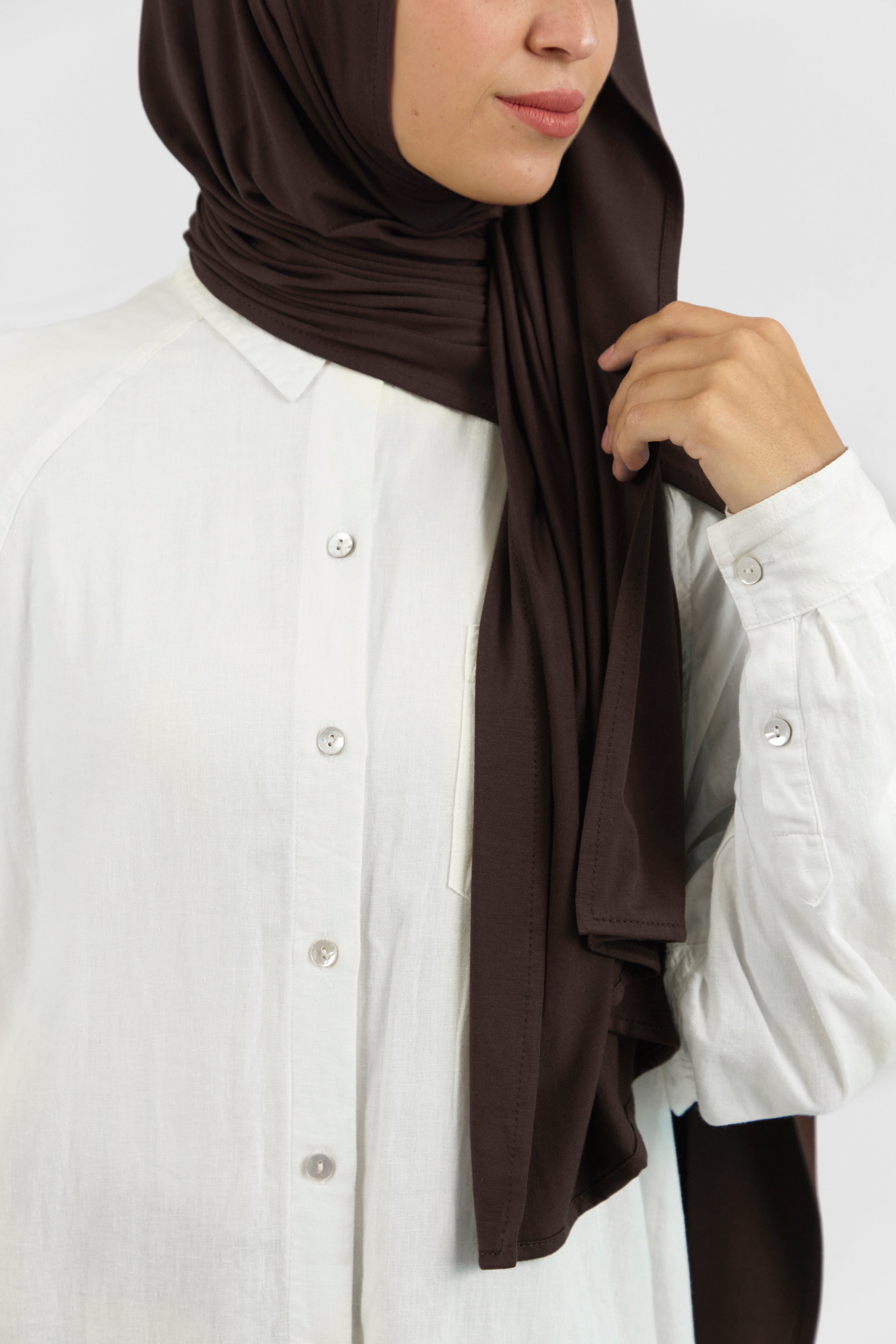 A close-up of a woman wearing a matching jersey hijab set. The model is turned to the right. Colour description: dark brown.