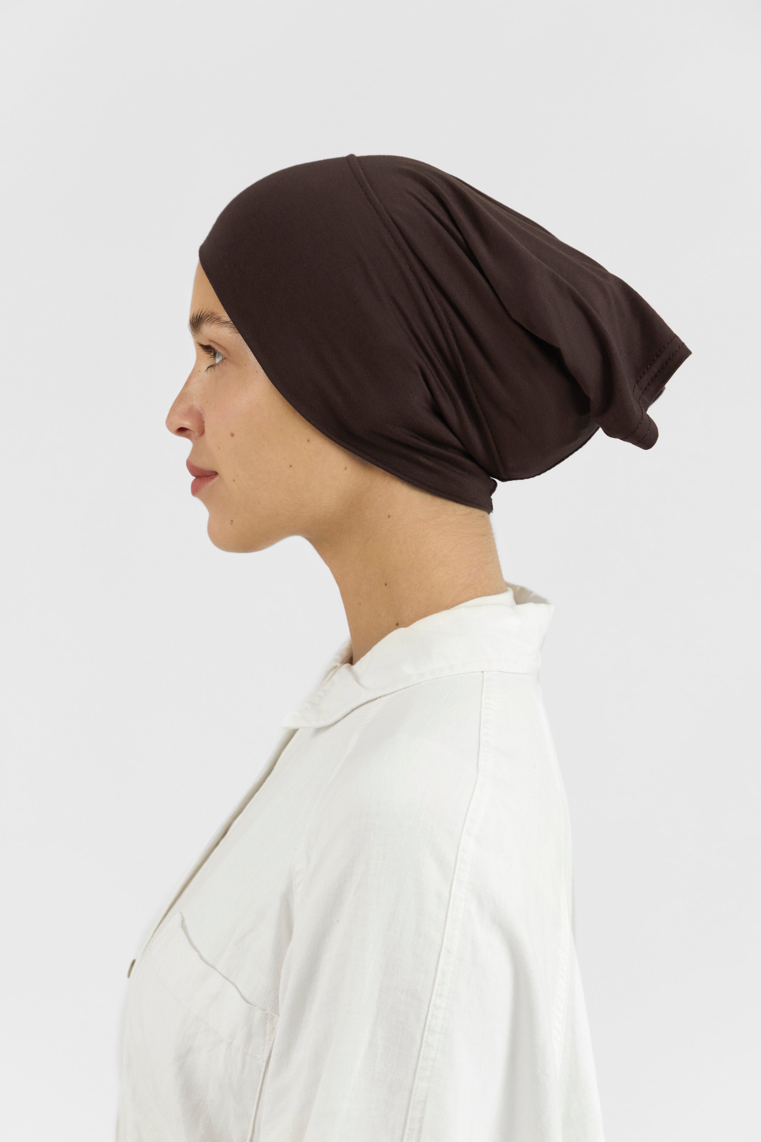 The left profile of a female model wearing a hijab undercap. Colour description: dark brown.