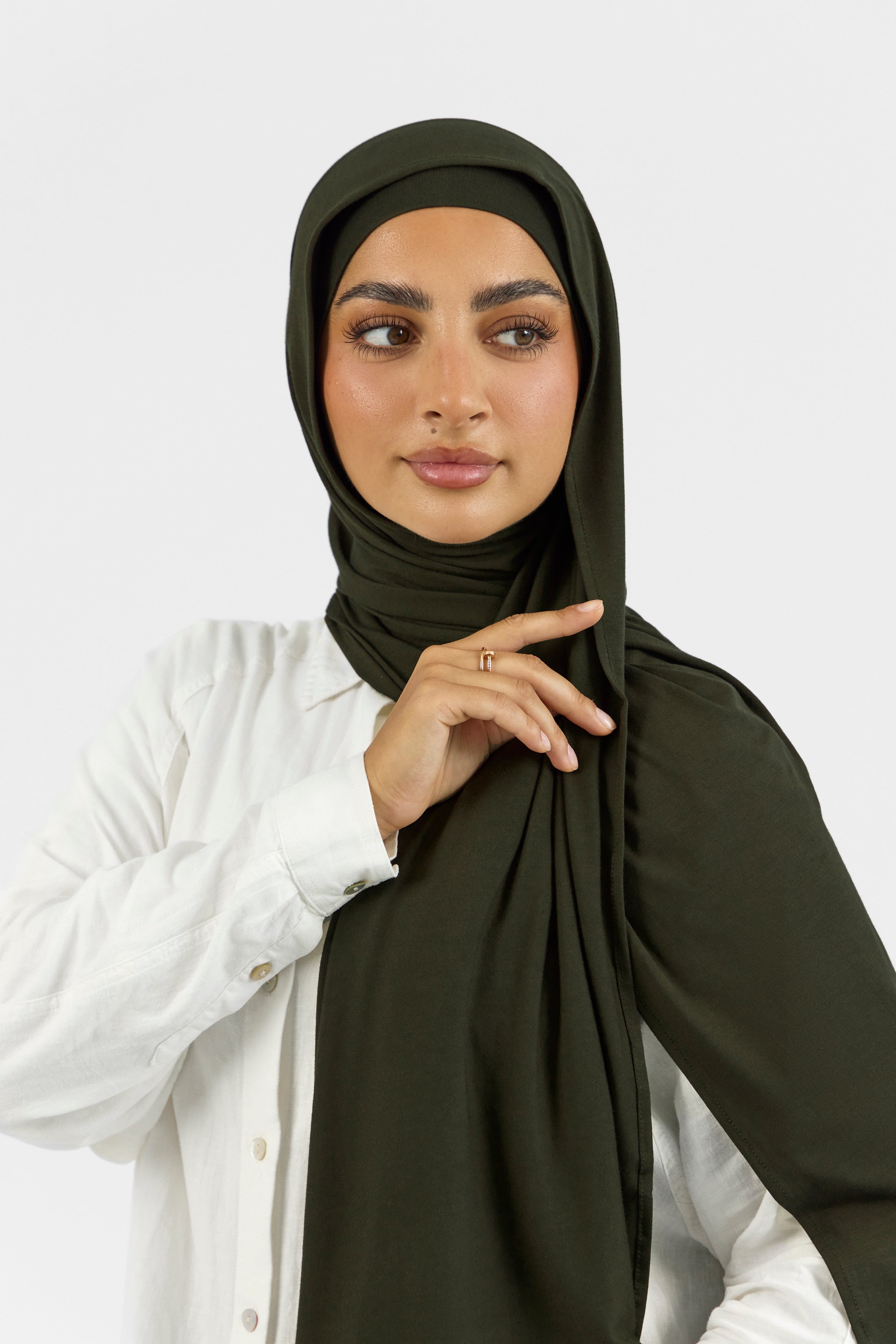 A female model touching the matching jersey hijab set she wears. Colour description: dark green.