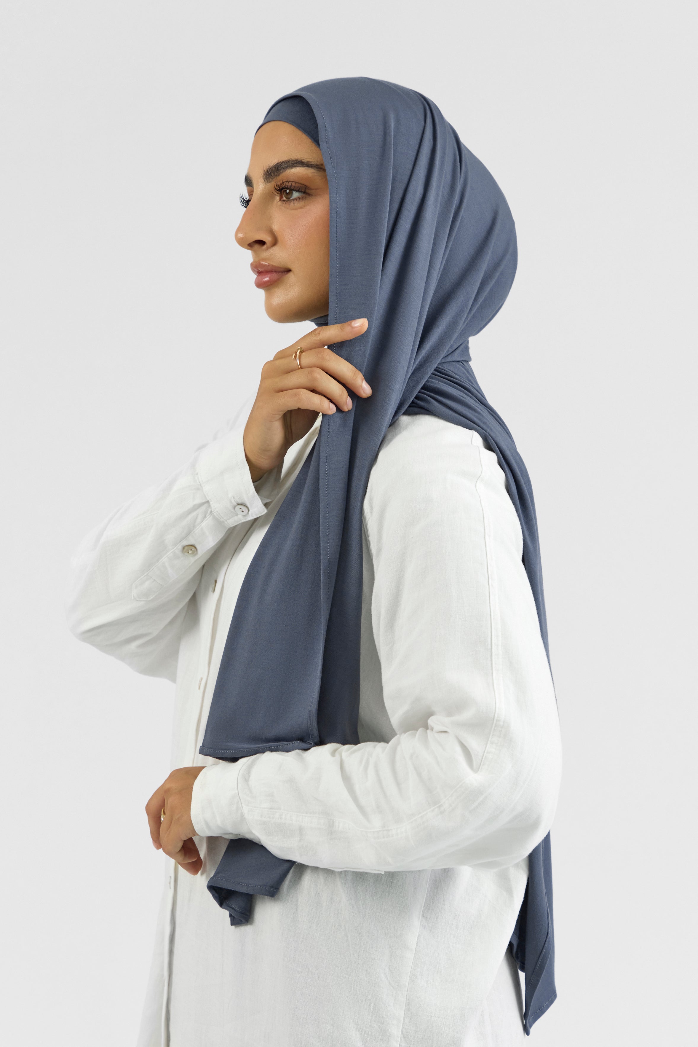 A female model wearing a matching jersey hijab set. The model is turned to the left. This set includes a modal jersey hijab and matching undercap. Colour description: denim blue.