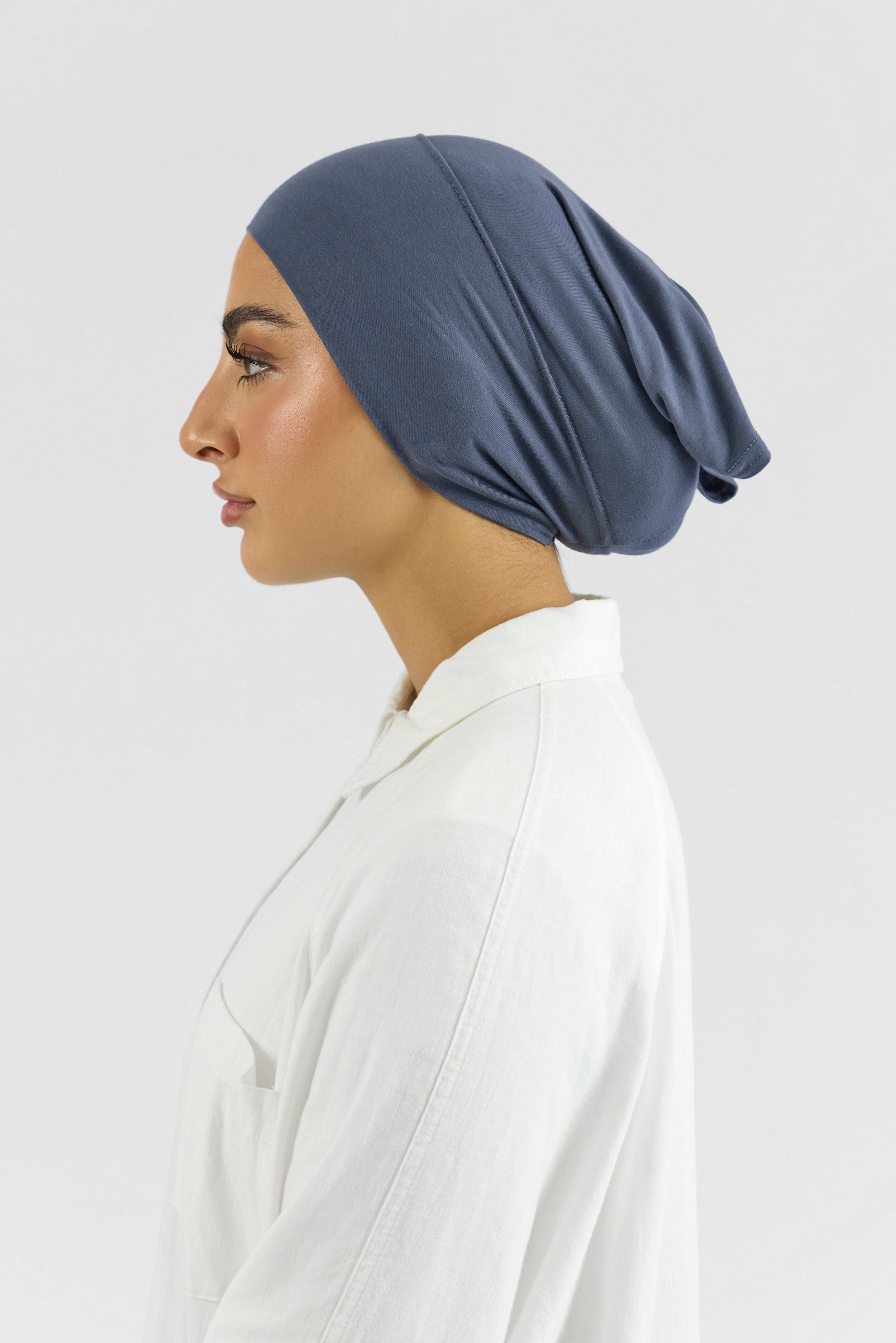 The left profile of a female model wearing a hijab undercap. Colour description: denim blue.