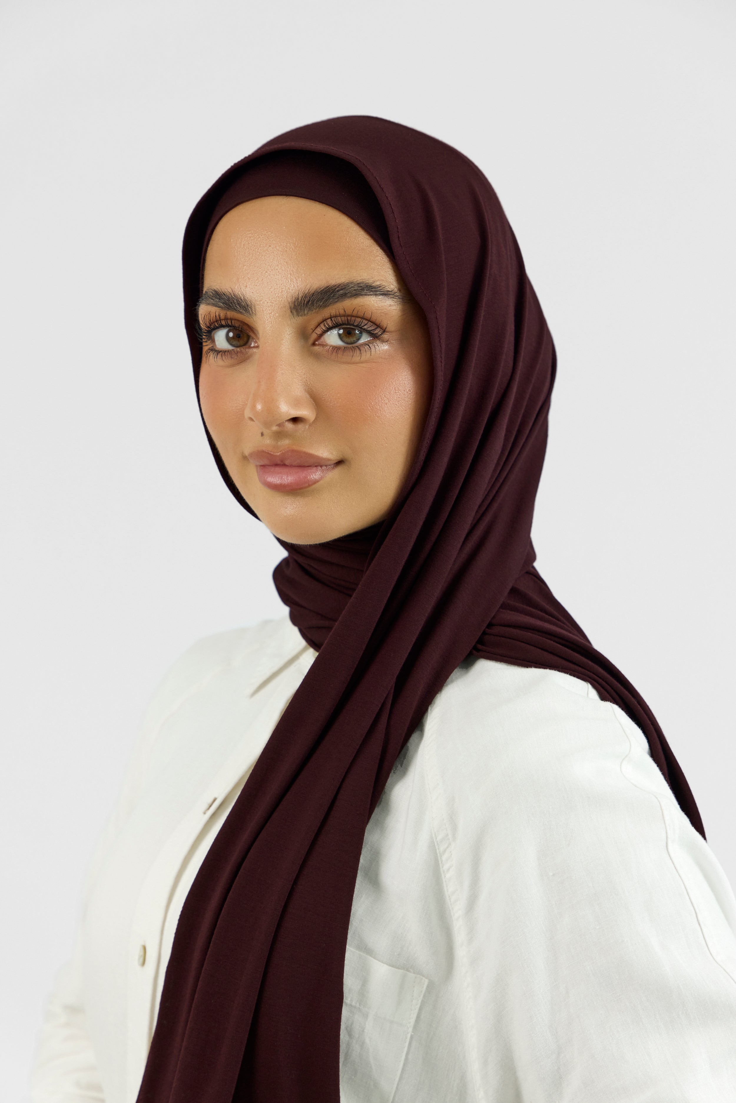 A woman wearing one of FARES's matching jersey hijab sets. The model is turned to the left. Colour description: deep plum.