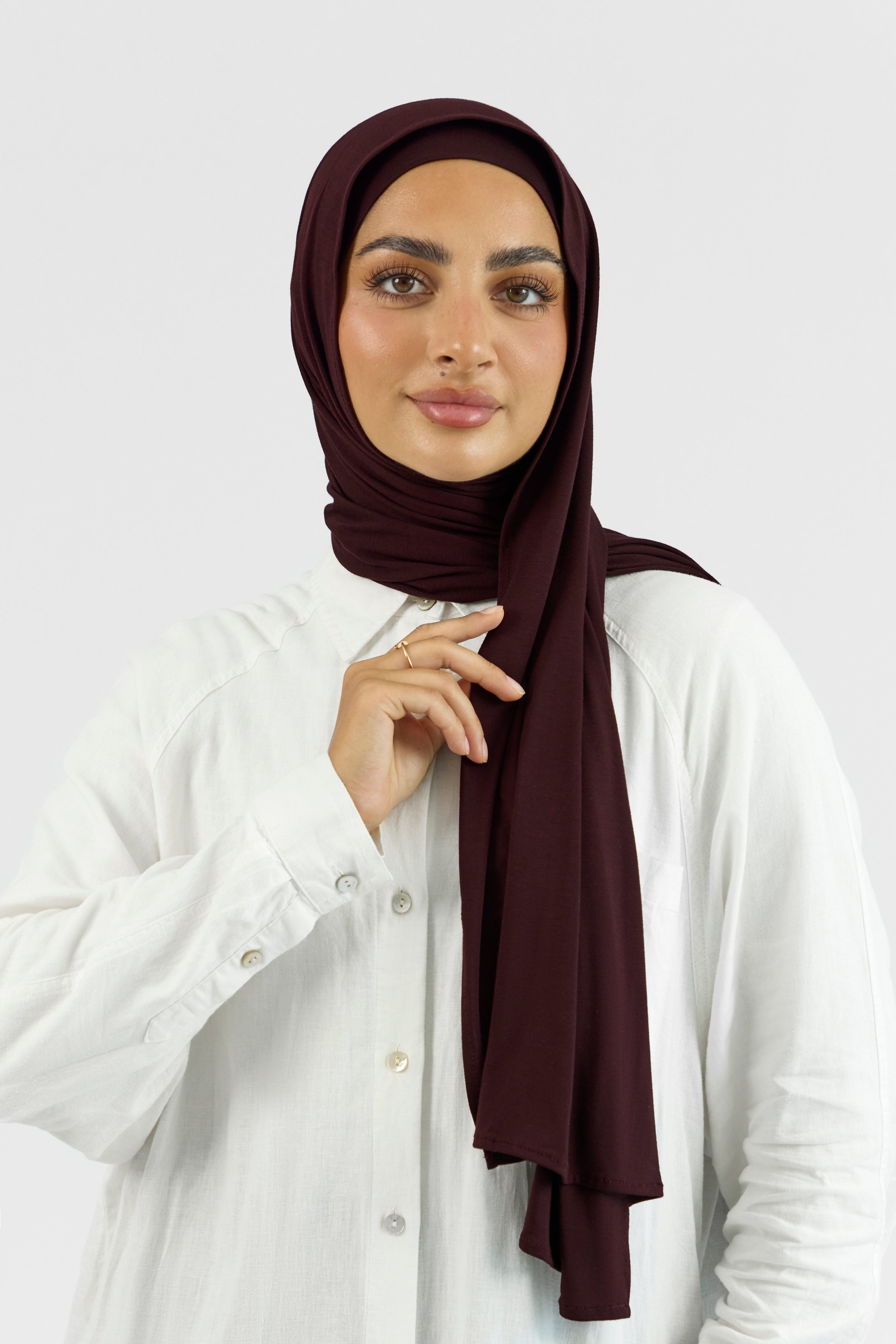 A woman wearing one of FARES's matching jersey hijab sets. Colour description: deep plum. This set includes a modal jersey hijab and matching undercap.