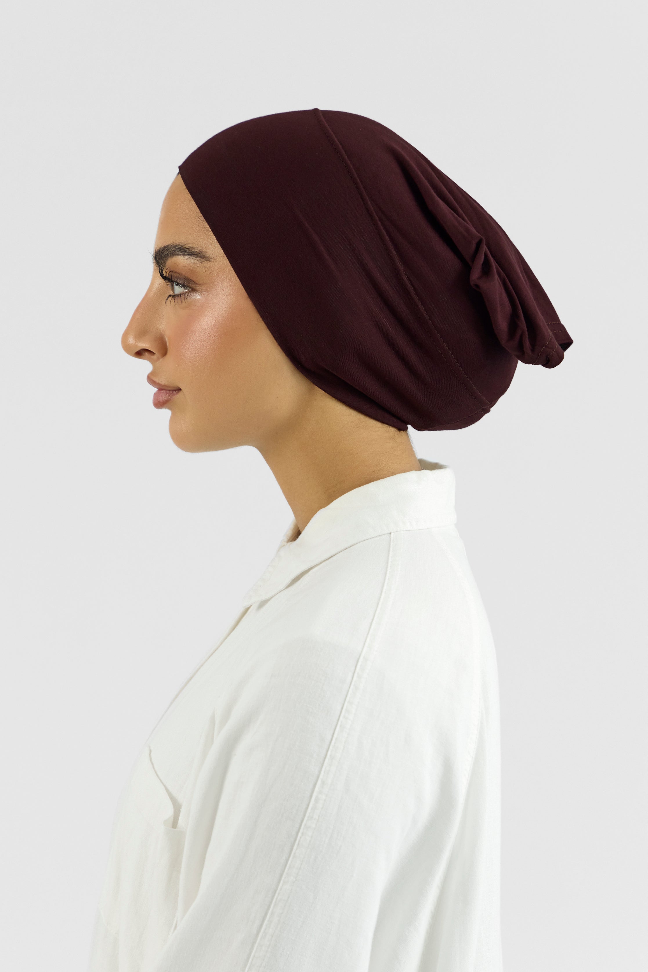 The left profile of a female model wearing a hijab undercap. Colour description: deep plum.