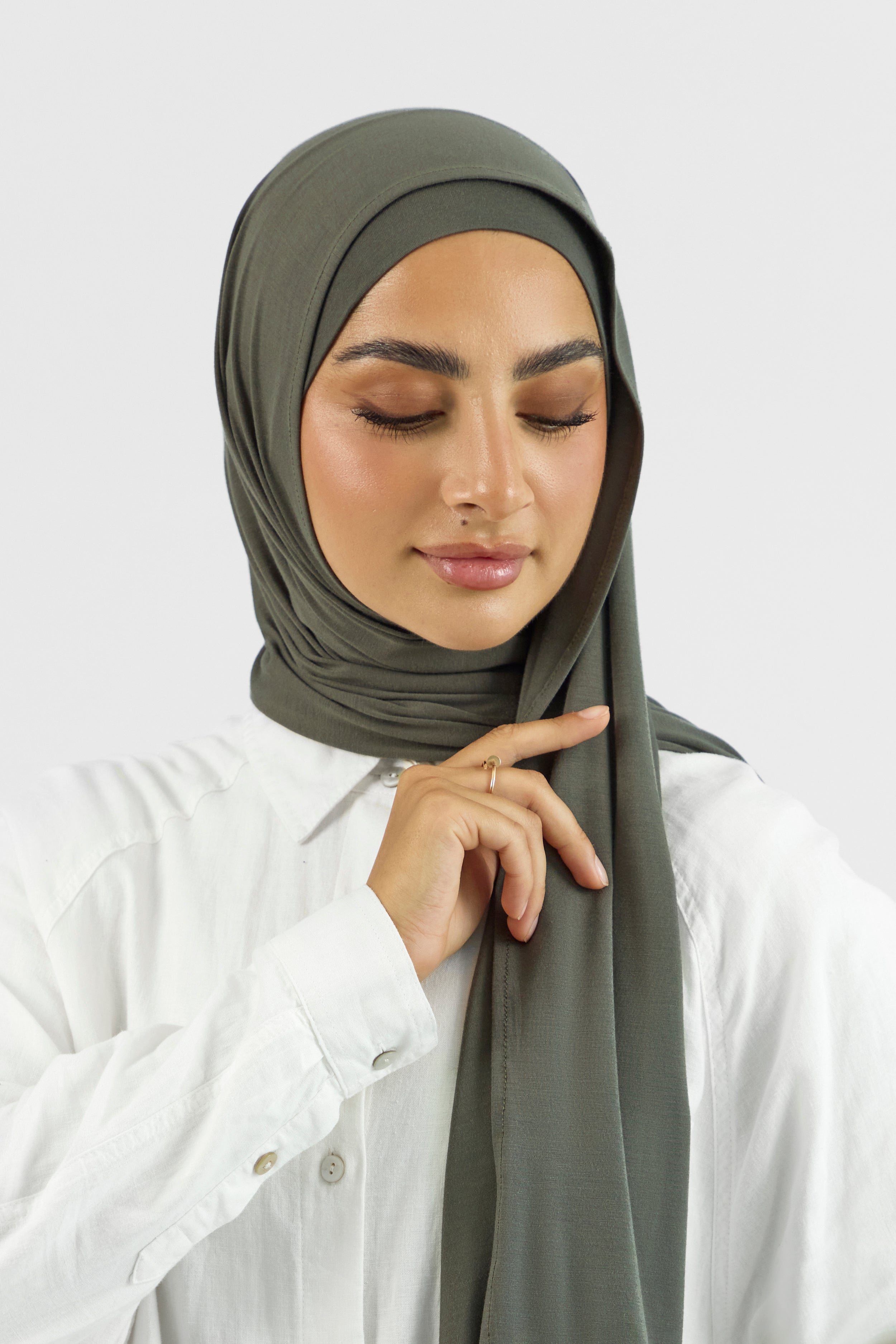 A close-up of the front of a female model touching the matching jersey hijab set she wears. Colour description: muted green.