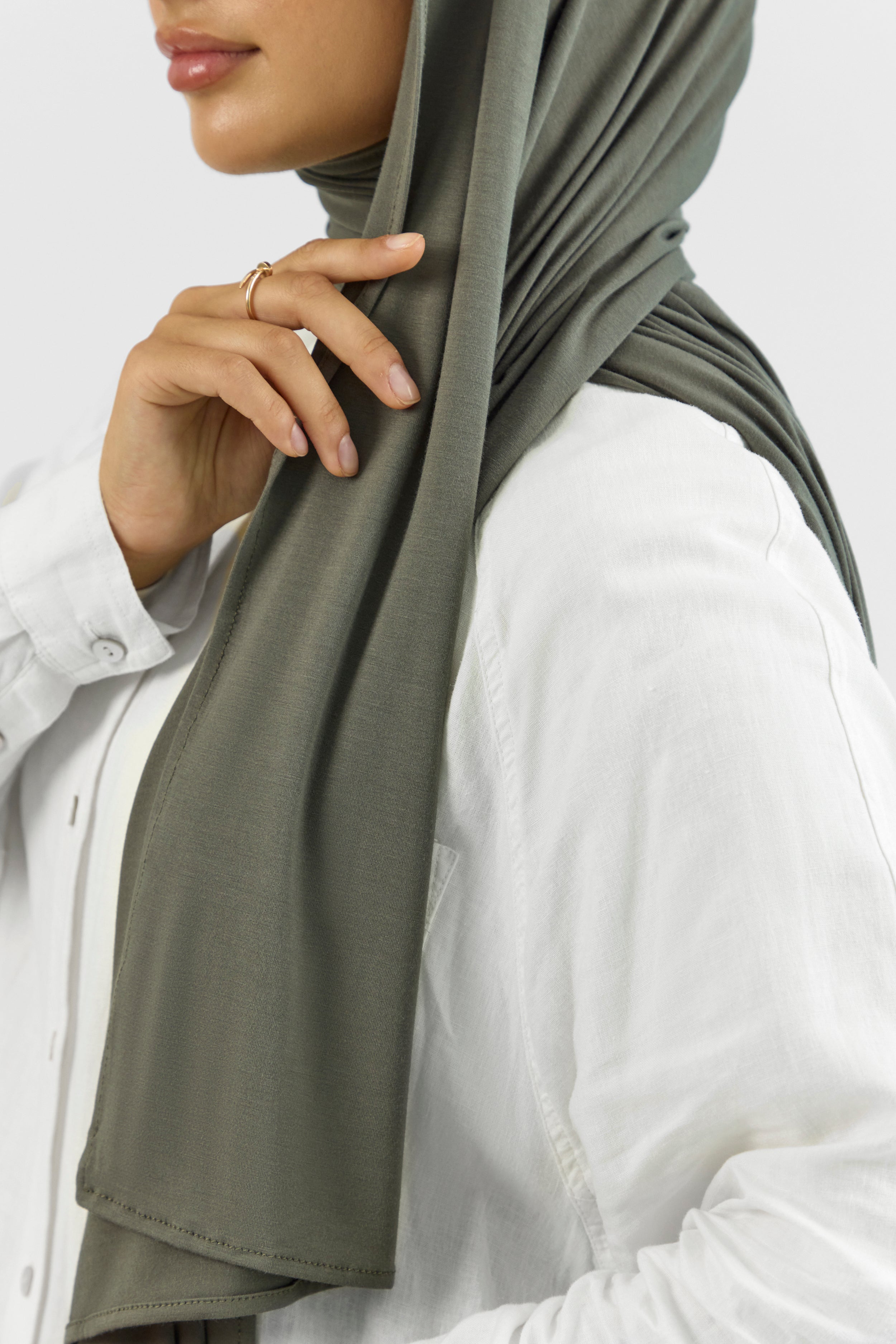 A close-up of a woman wearing one of FARES's matching jersey hijab sets. The model is turned to the left. Colour description: muted green.