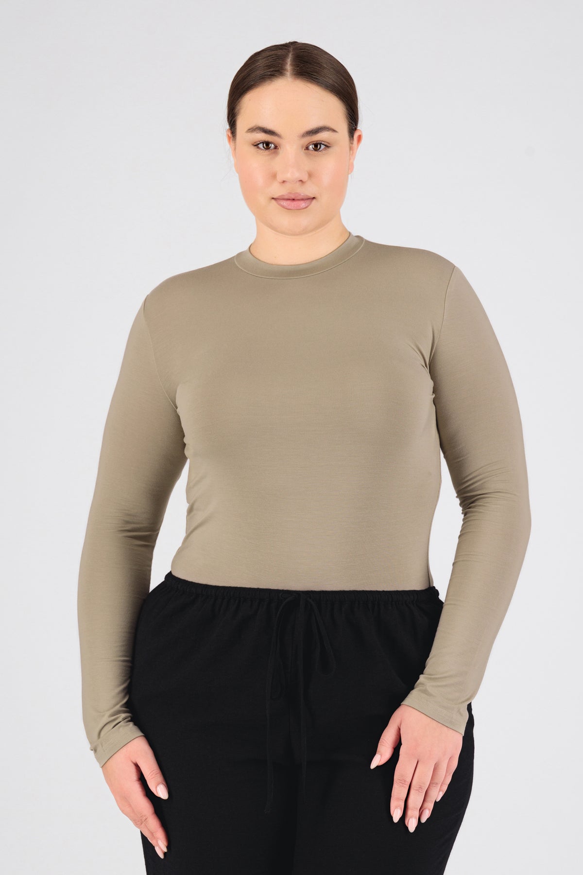 A model is wearing FARES' long sleeve layer. Colour description: Sand. She is standing with her front to the camera in a base layer with her hands on her thighs.
