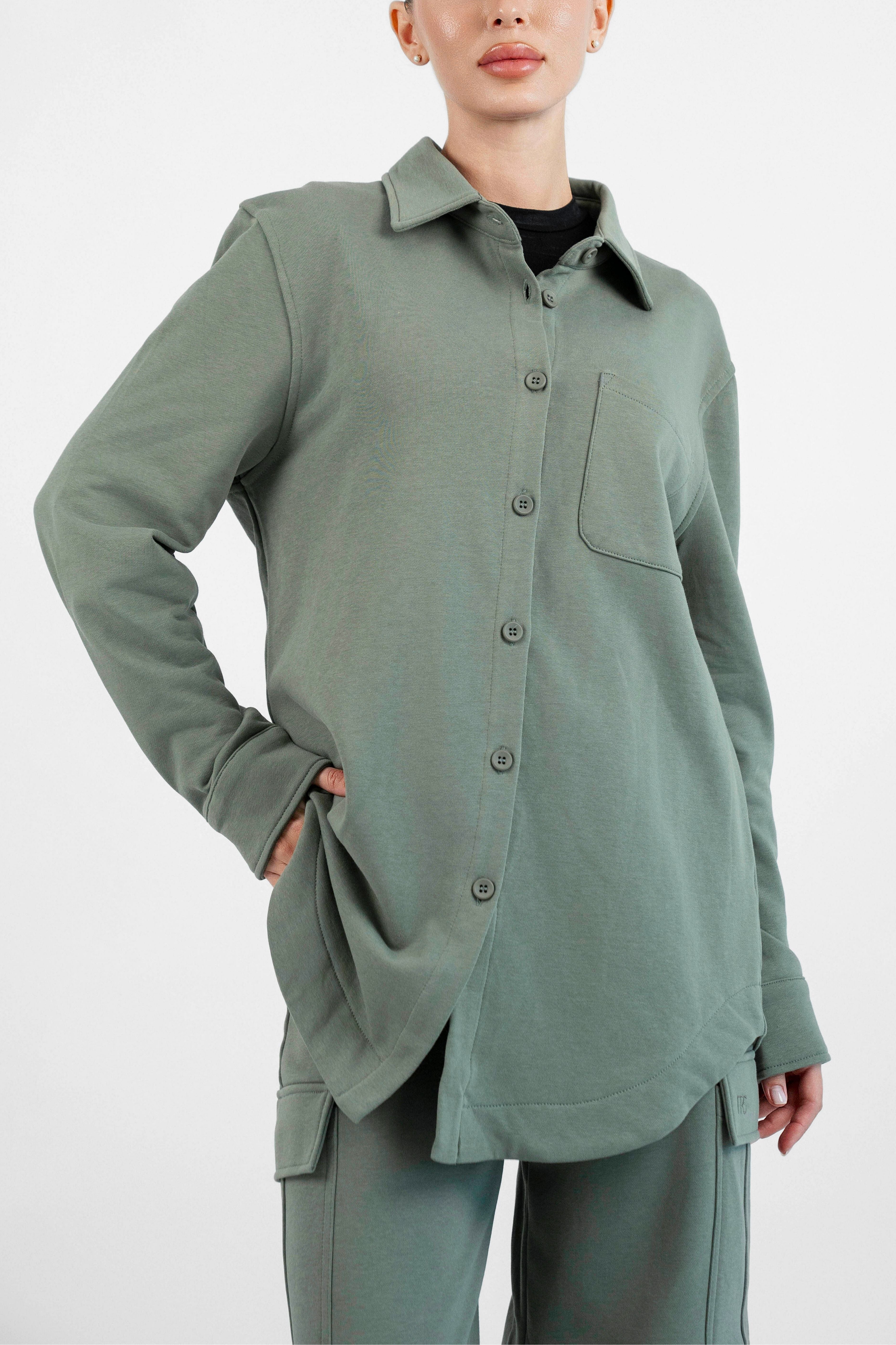Colour: Oakmoss. A close up of model posing with her hand in her pocket in an Oversized Cotton Shacket.