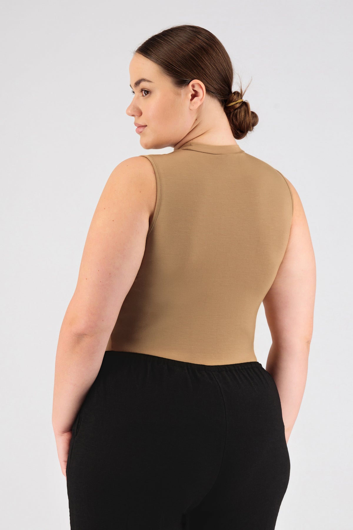 A girl wearing FARES' sleeveless layer is shown from the back while looking over her left shoulder. Colour description: Tan.