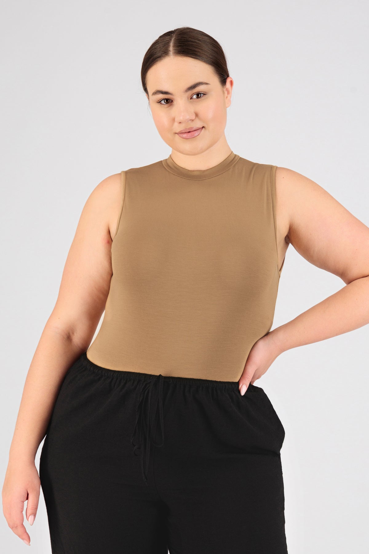 A model is facing the camera while wearing FARES' sleeveless layer. Her hand is on her hip. Colour description: Tan.