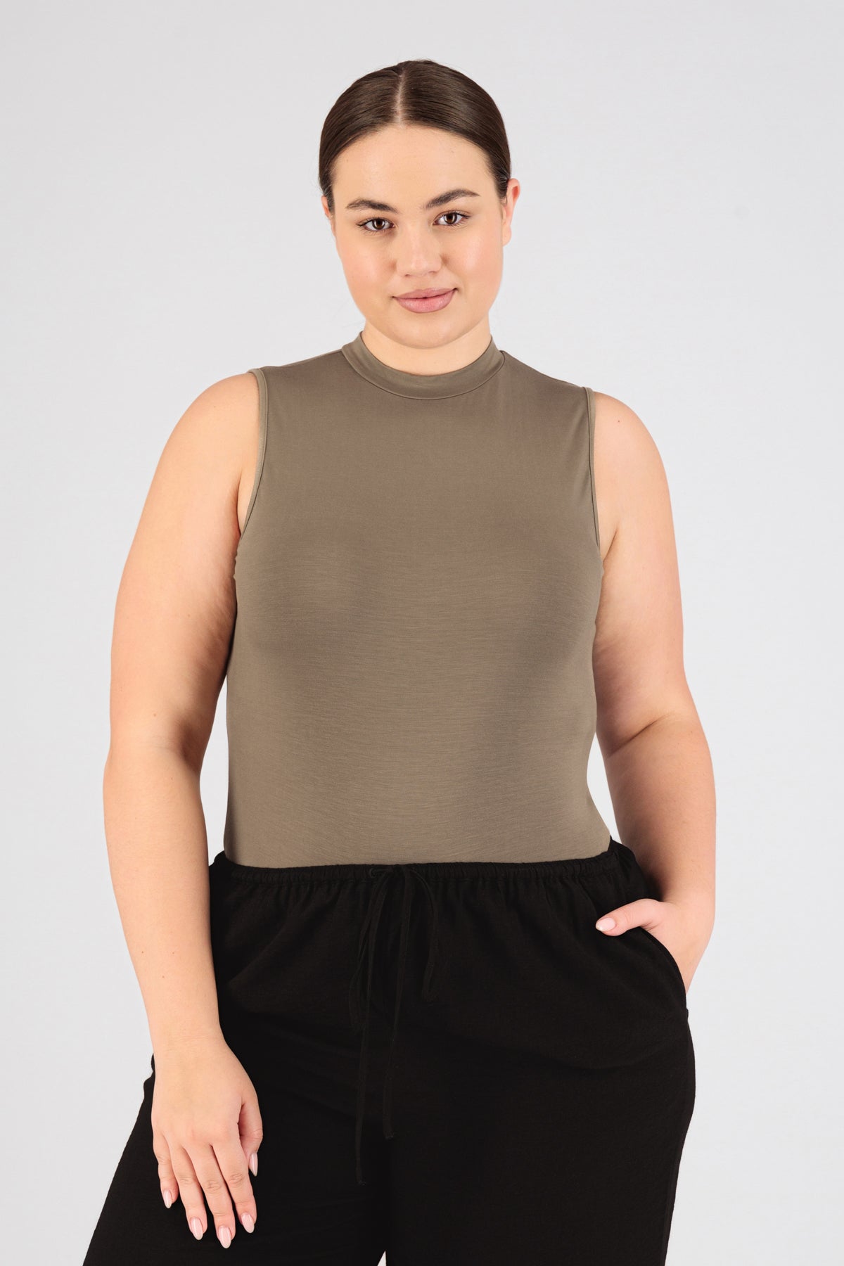 A girl is wearing FARES' sleeveless layer. She is standing in the sleevless top with her left hand in her pocket. Colour description: Taupe.
