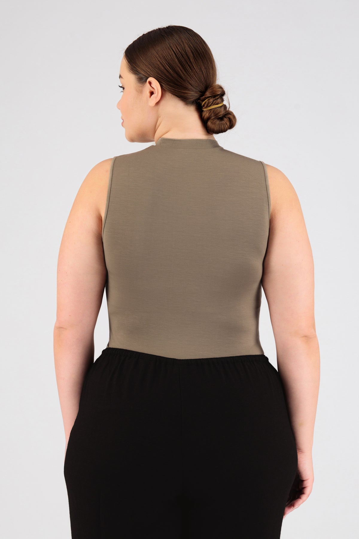 The model wearing FARES' sleeveless layer is shown from the back. Her head is turned to the left. Colour description: Taupe.