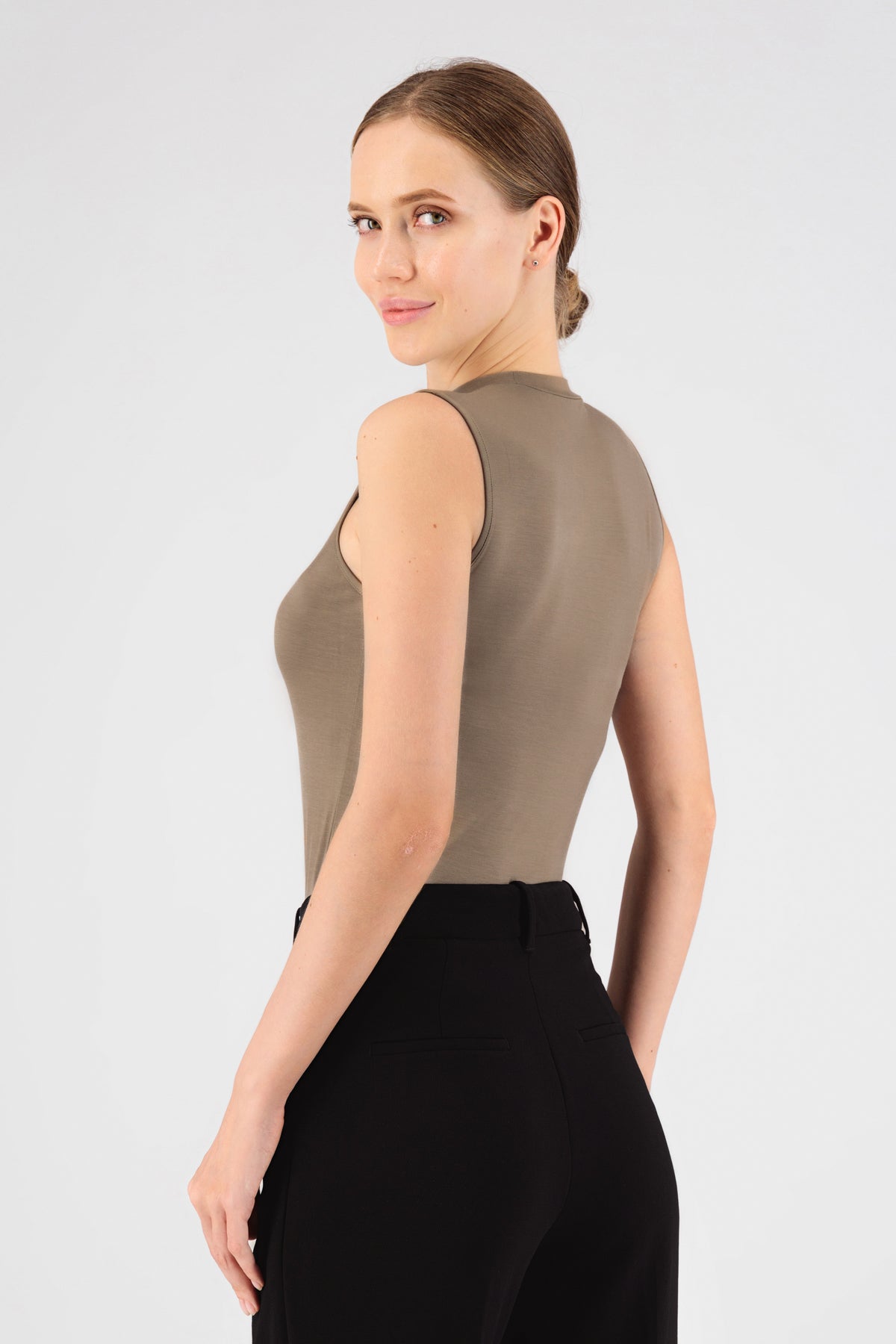 The girl wearing FARES' sleeveless layer is shown from the back. She is looking back over her left shoulder. Colour description: Taupe.