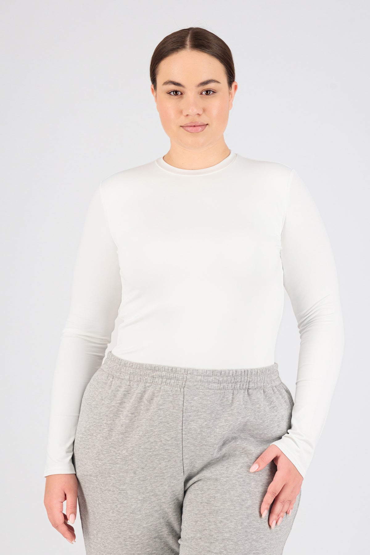 A girl is wearing FARES' long sleeve layer. Colour description: White. She is standing with her front to the camera in a fitted long sleeve base layer.