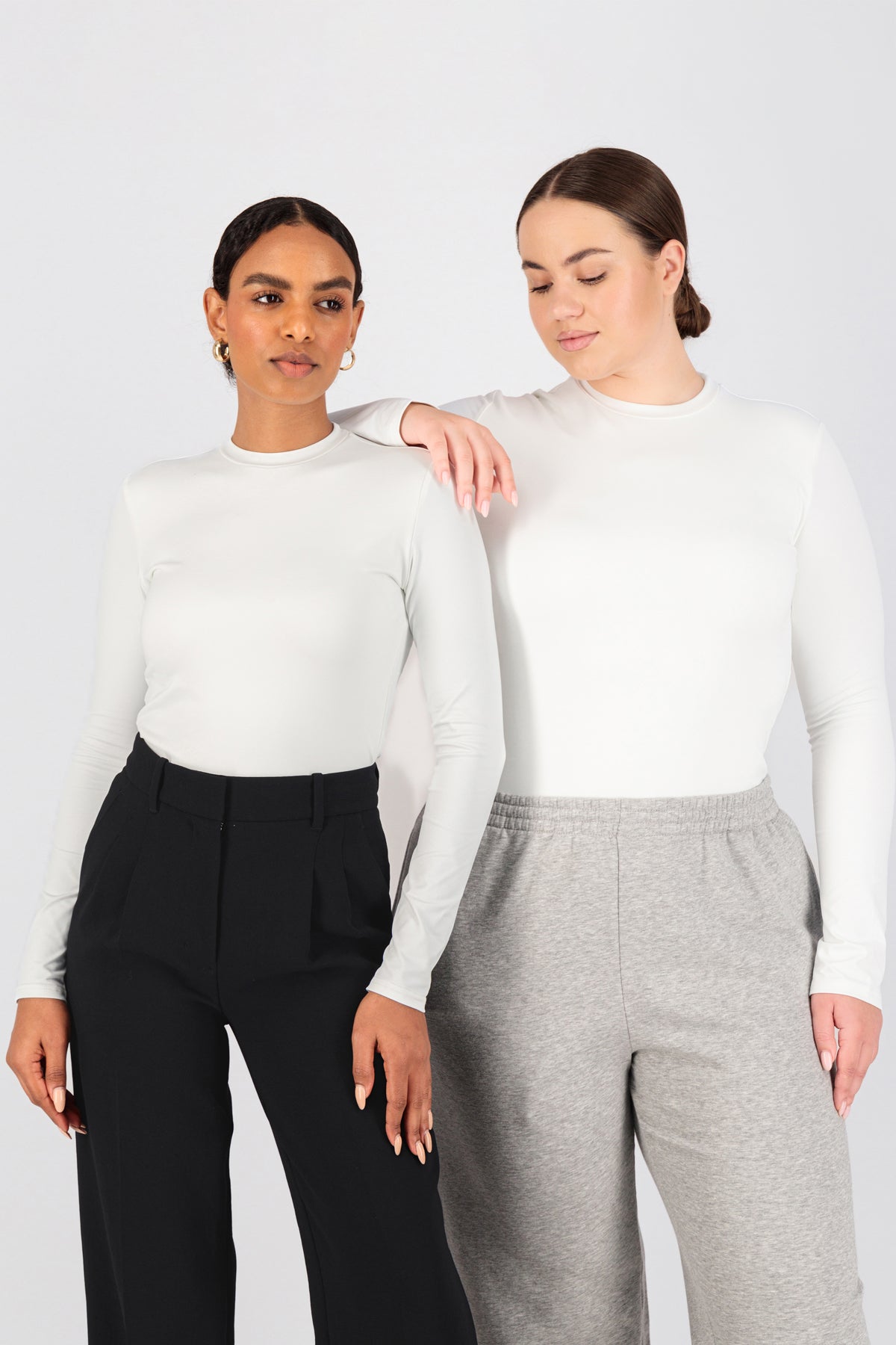 Two girls are standing side by side in FARES' best base layer clothing. Colour description: White. One of the girls is resting her hand on the other girl's shoulder.