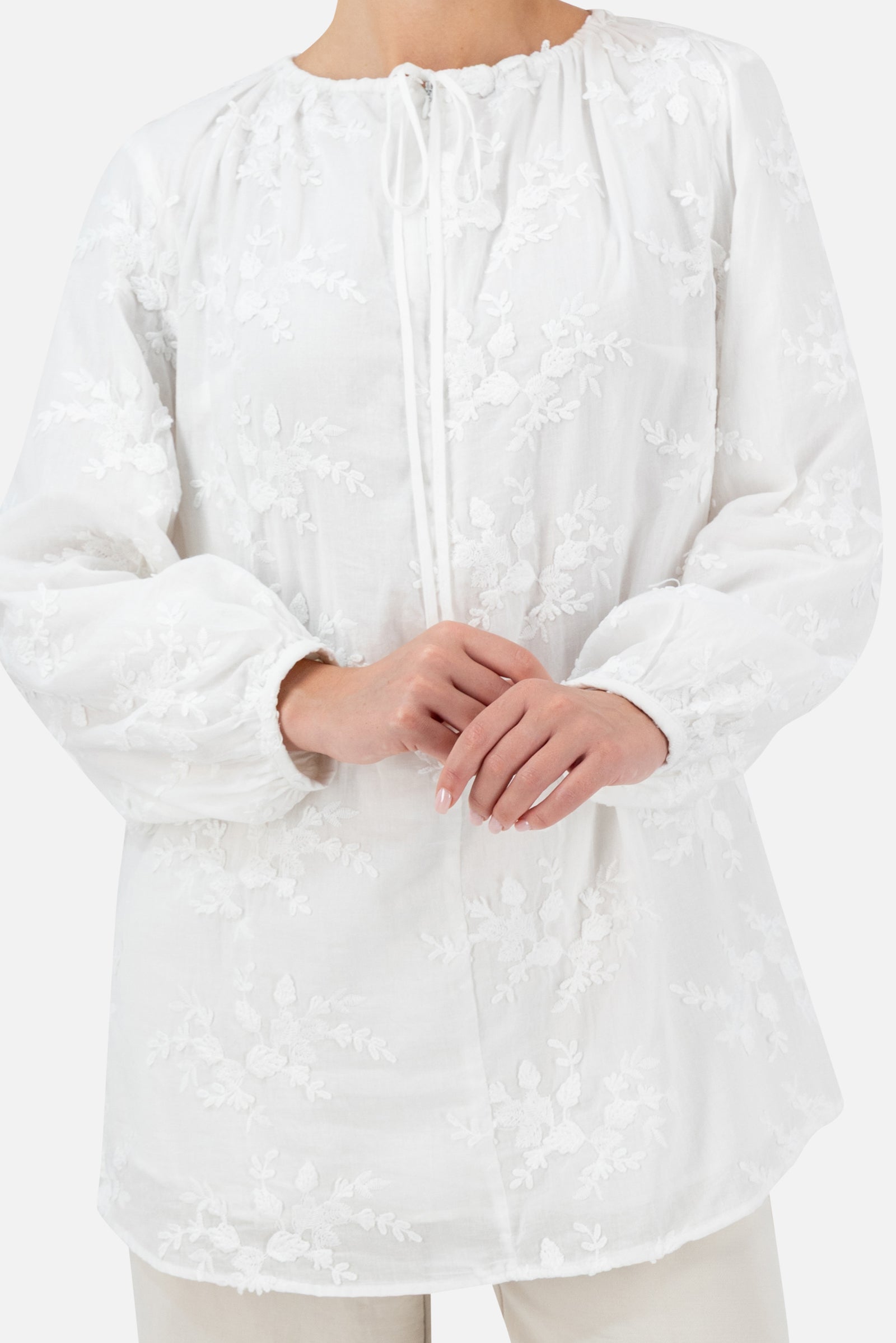 Close-up of the white floral embroidered blouse with the model's hands folded.