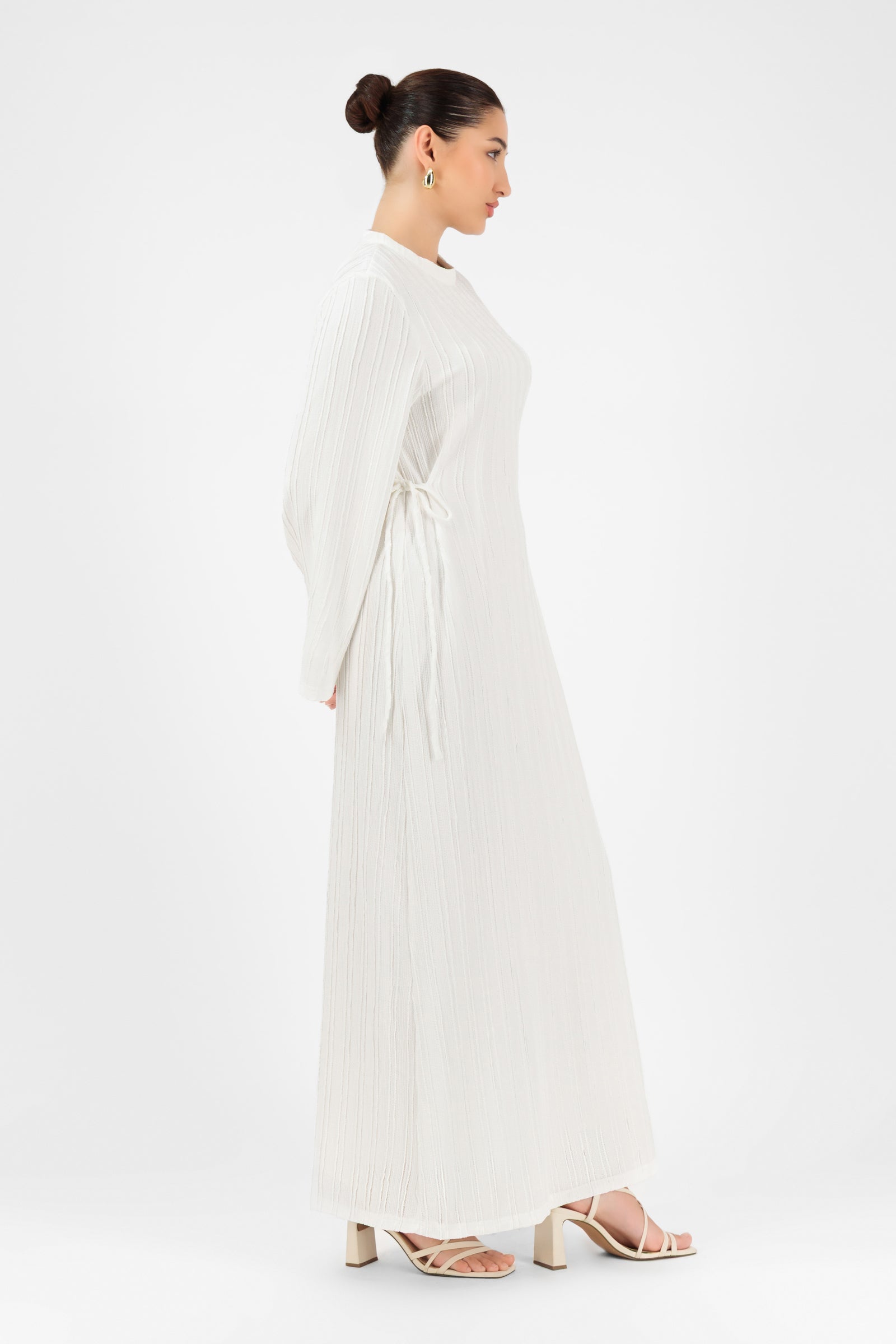 Side profile of a model wearing the FARES Textured Bow Detail Dress in White styled as a graceful maxi dresses look.