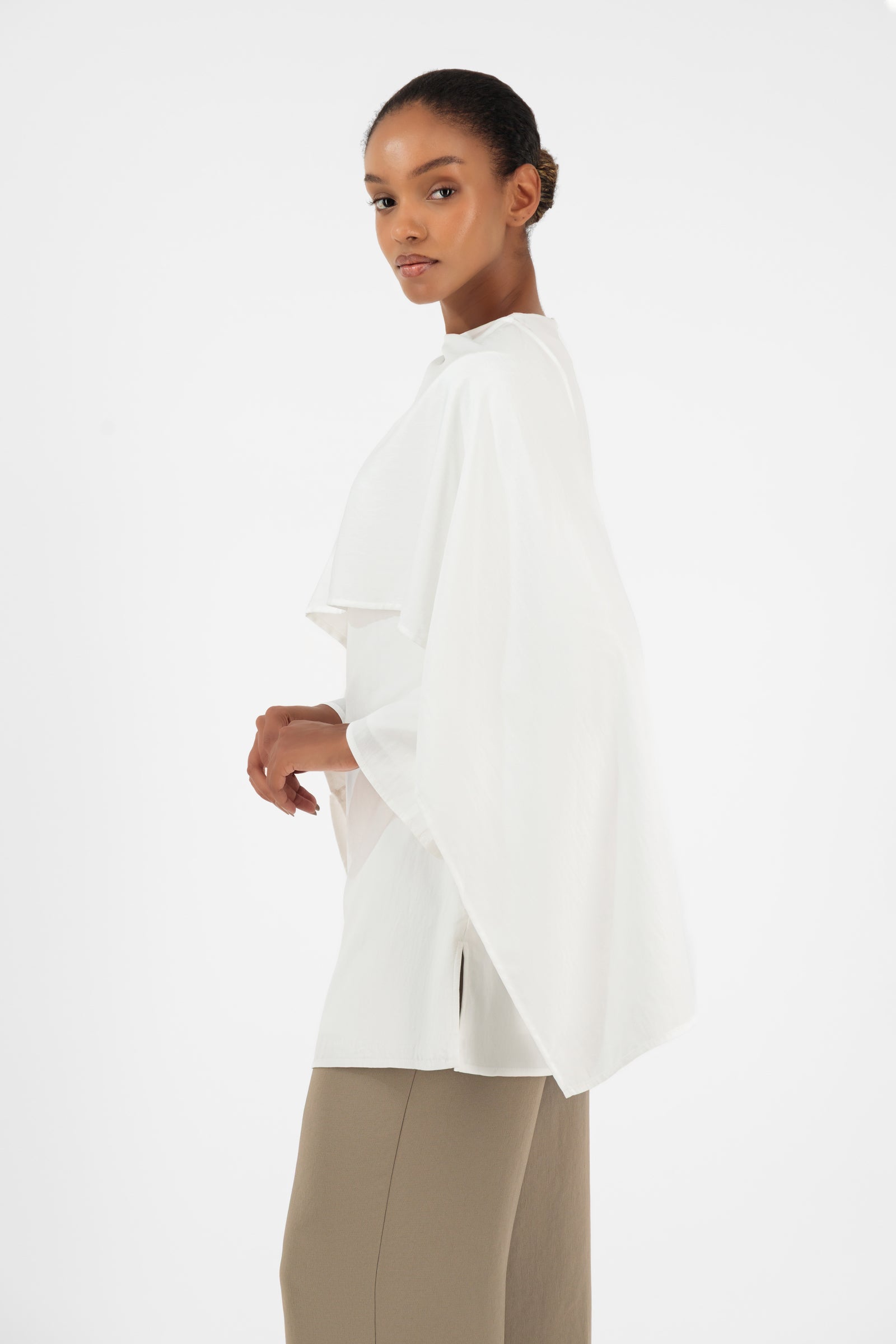 Side profile of the FARES Cape Overlay Tunic in White highlighting the graceful drape and modern button-up inspired styling.