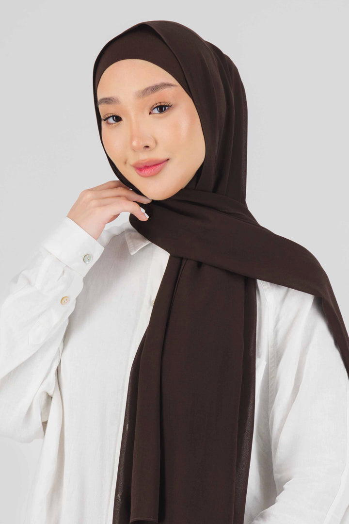 A close-up of the front of a female model touching the matching chiffon hijab set she wears. Colour description: dark brown.
