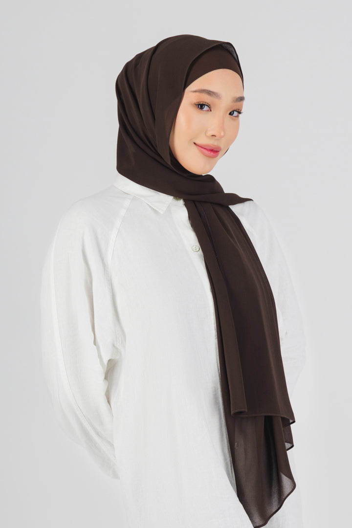 A female model wearing a matching chiffon hijab set. The model is turned to the right. This hijab fashion wear includes a high quality chiffon hijab and a breathable matching modal jersey undercap. Colour description: dark brown.