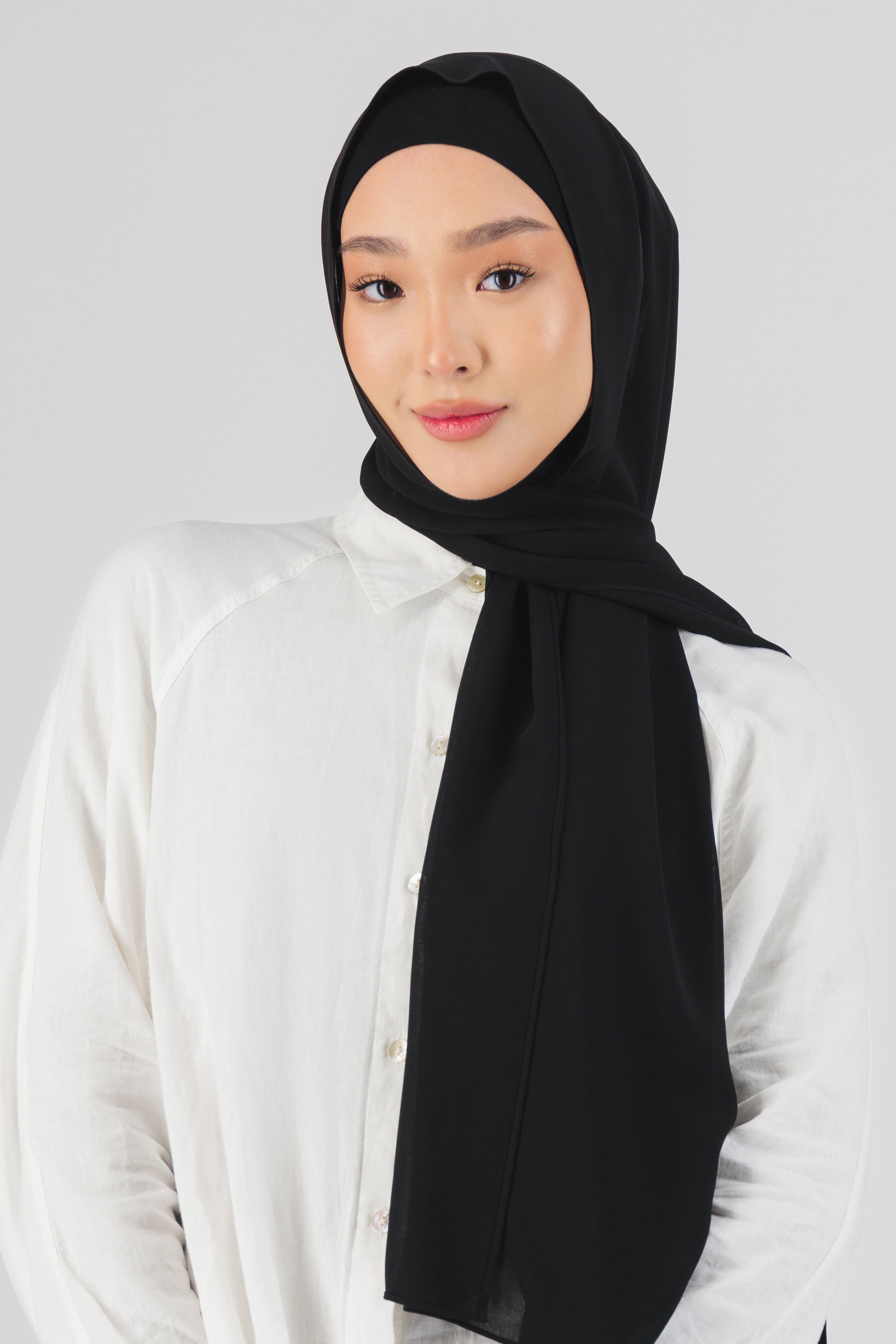 A close-up of the front of a female model wearing a matching chiffon hijab set. Colour description: black.