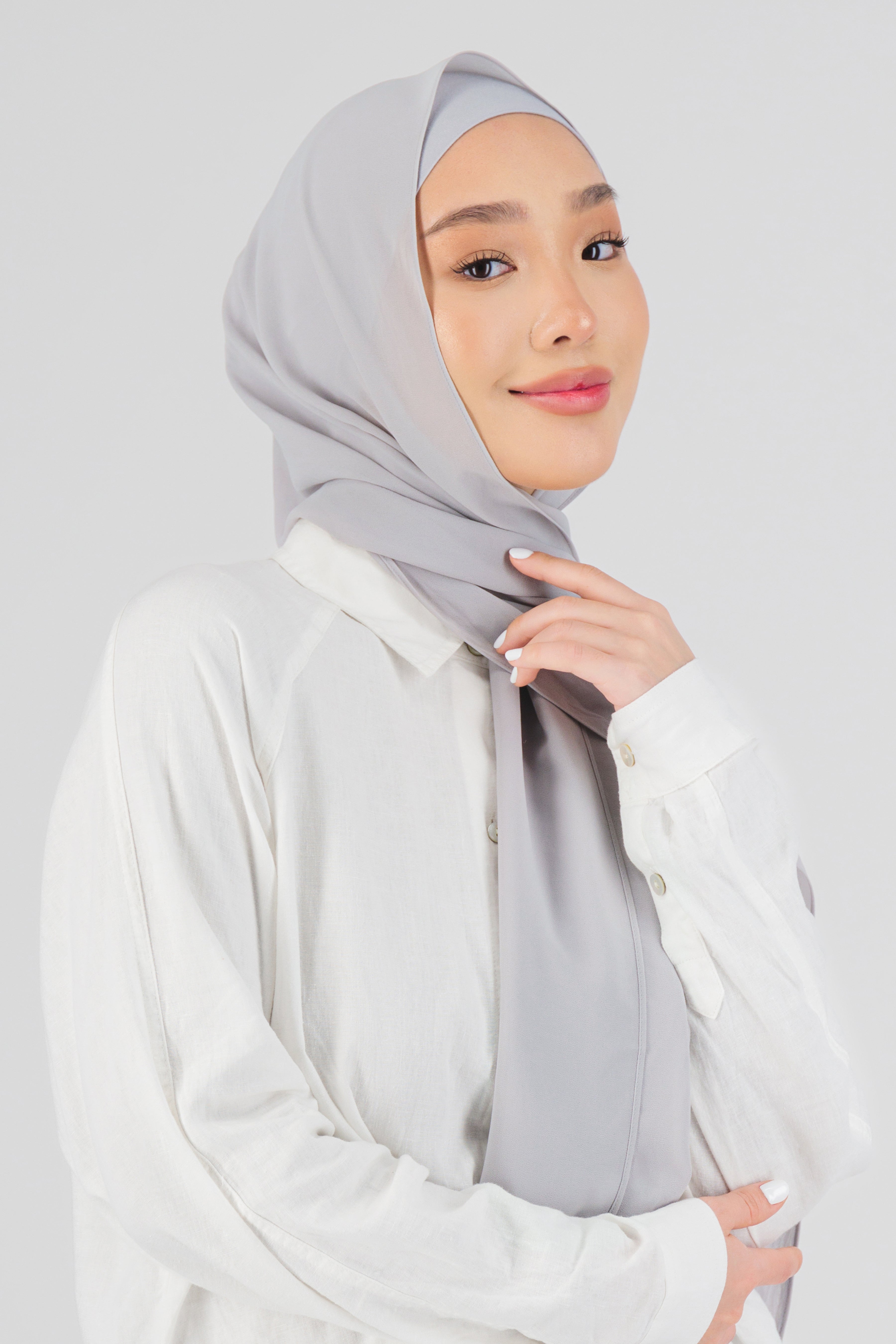 A woman wearing one of FARES's matching chiffon hijab sets. The model is turned to the right. Colour description: light grey.