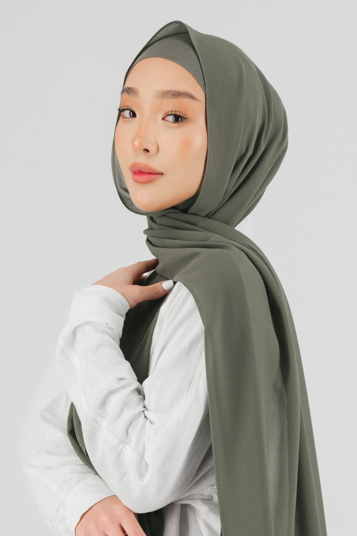 A female model wearing a matching chiffon hijab set. The model is standing side ways and looking over her left shoulder. Colour description: medium green.