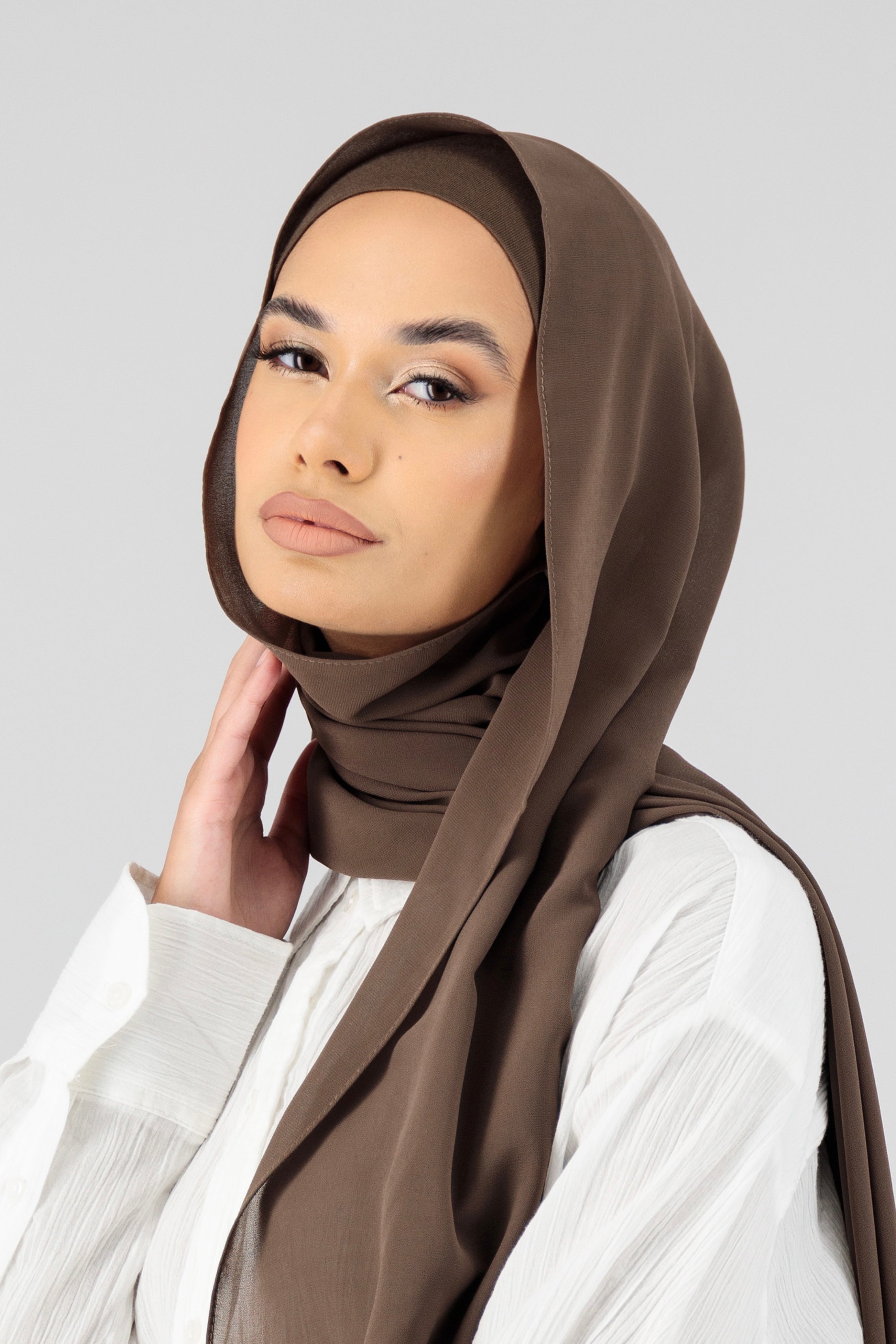 A female model wearing a matching chiffon hijab set. The model is turned to the left. Colour description: cool dark brown.