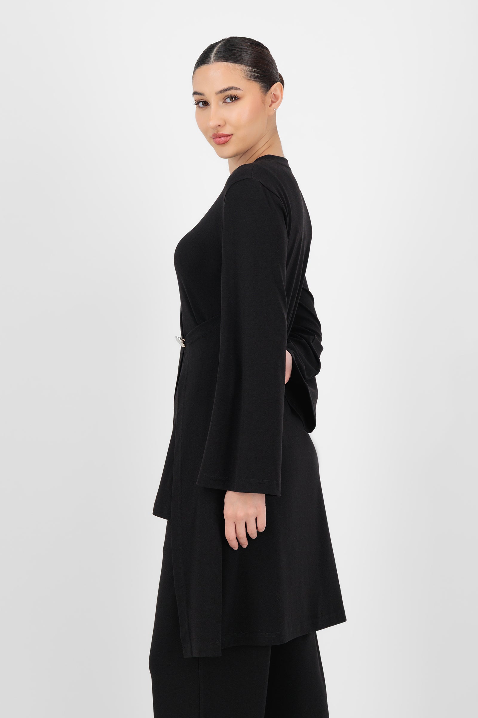 Side angle of the Gold Accent Wrap Top in Black showing the wrap silhouette, fitted sleeves, and soft fabric that define an elegant long sleeve wrap top.