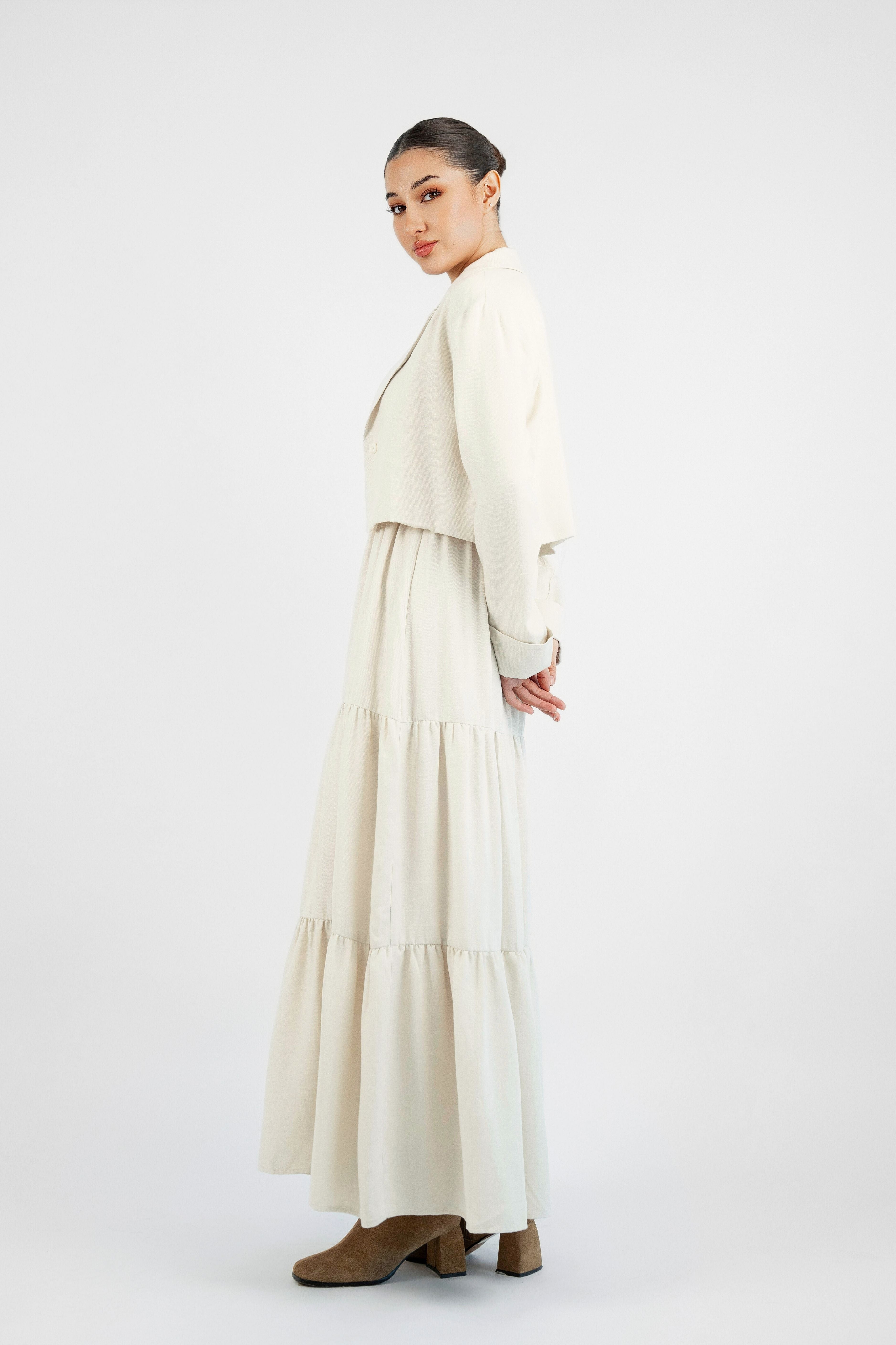 A girl turned to the left wearing a tiered dress and matching blazer set. Colour description: Cream.