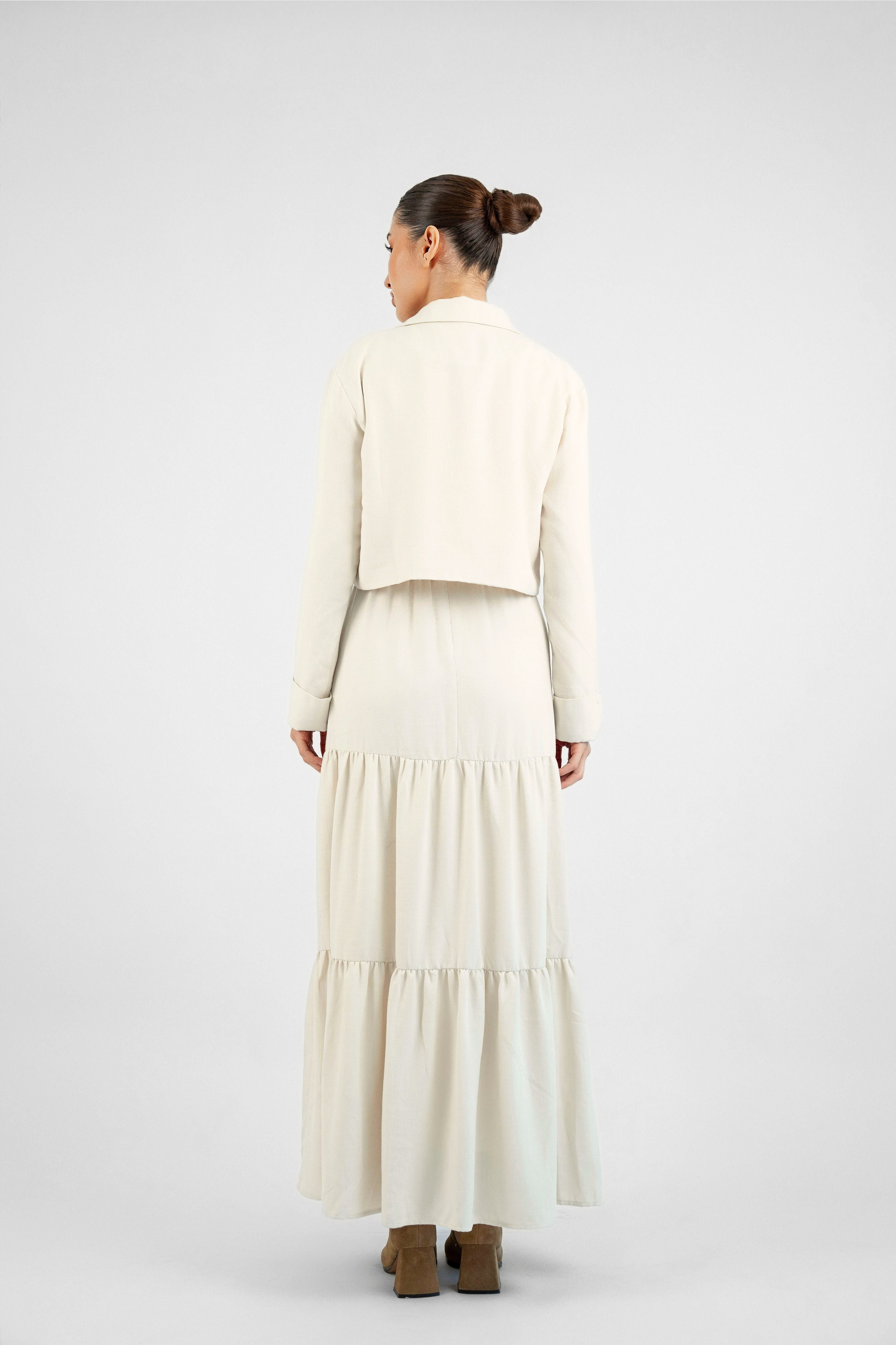 The model wearing a tiered dress and matching blazer set is shown from the back while looking over her left shoulder. Colour description: Cream