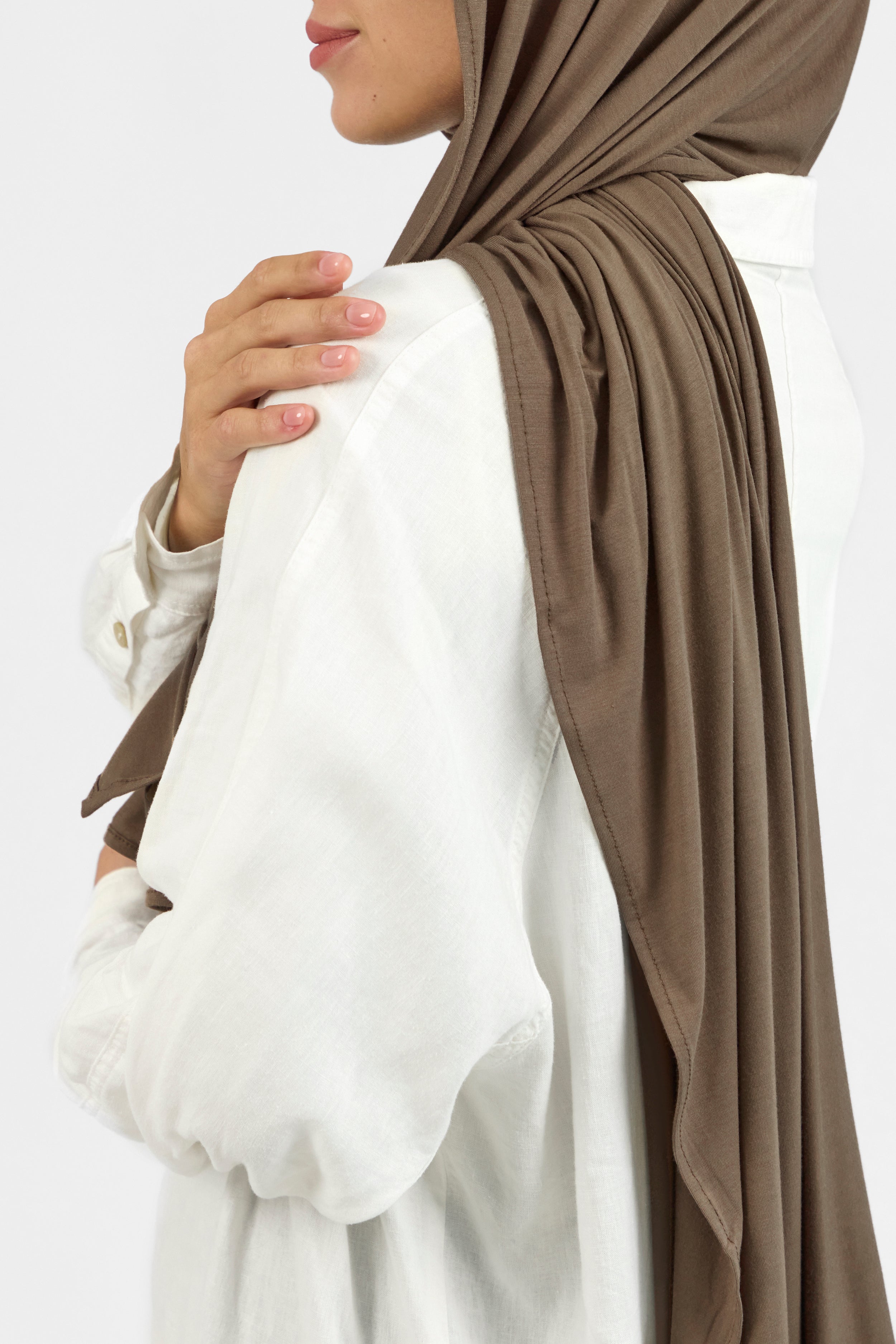 A close up of a female model looking back over her left shoulder with her hand on her shoulder wearing a matching jersey hijab set. This set includes a modal jersey hijab and matching undercap. Colour description: medium beige-brown.
