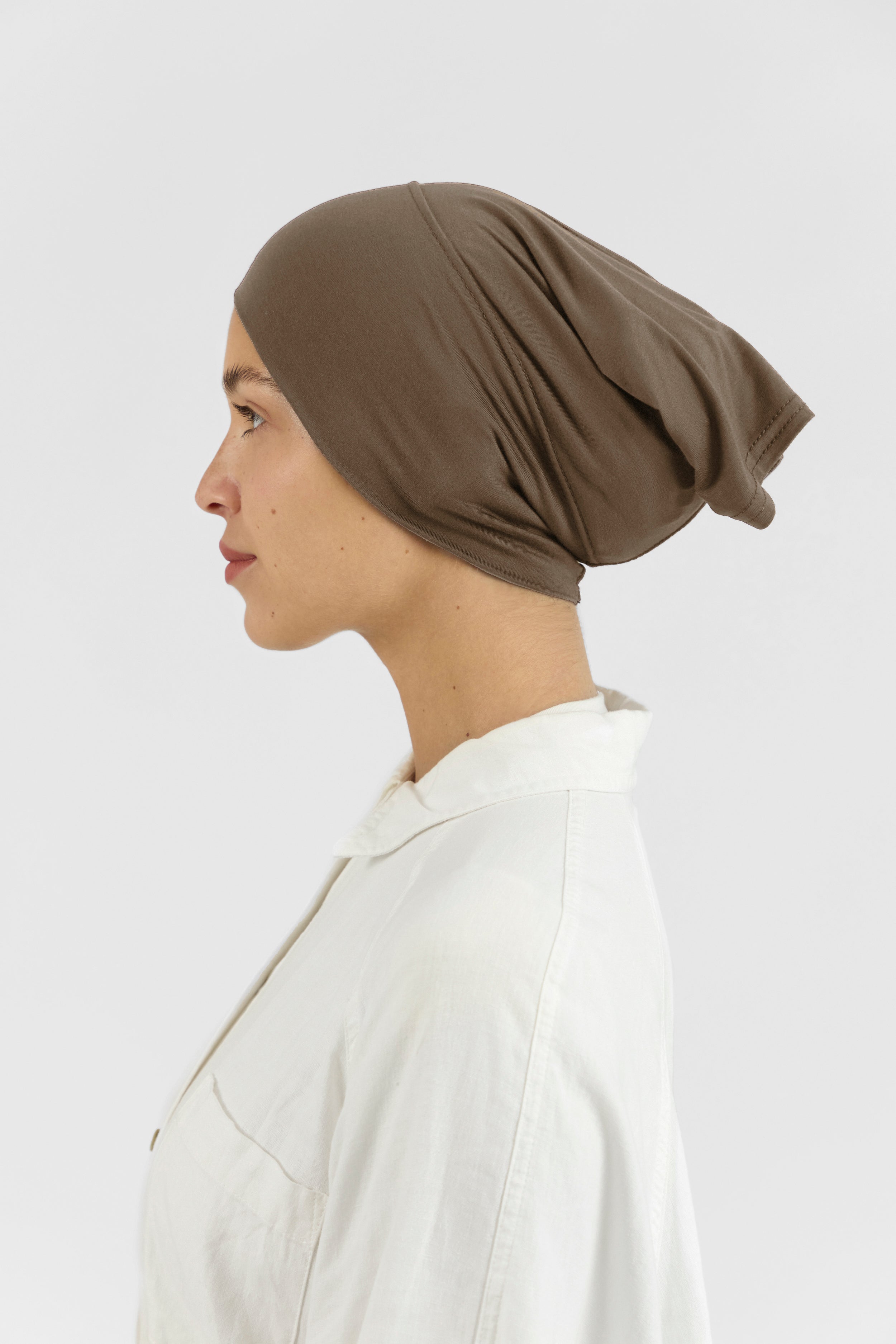 The left profile of a female model wearing a hijab undercap. Colour description: medium beige-brown.
