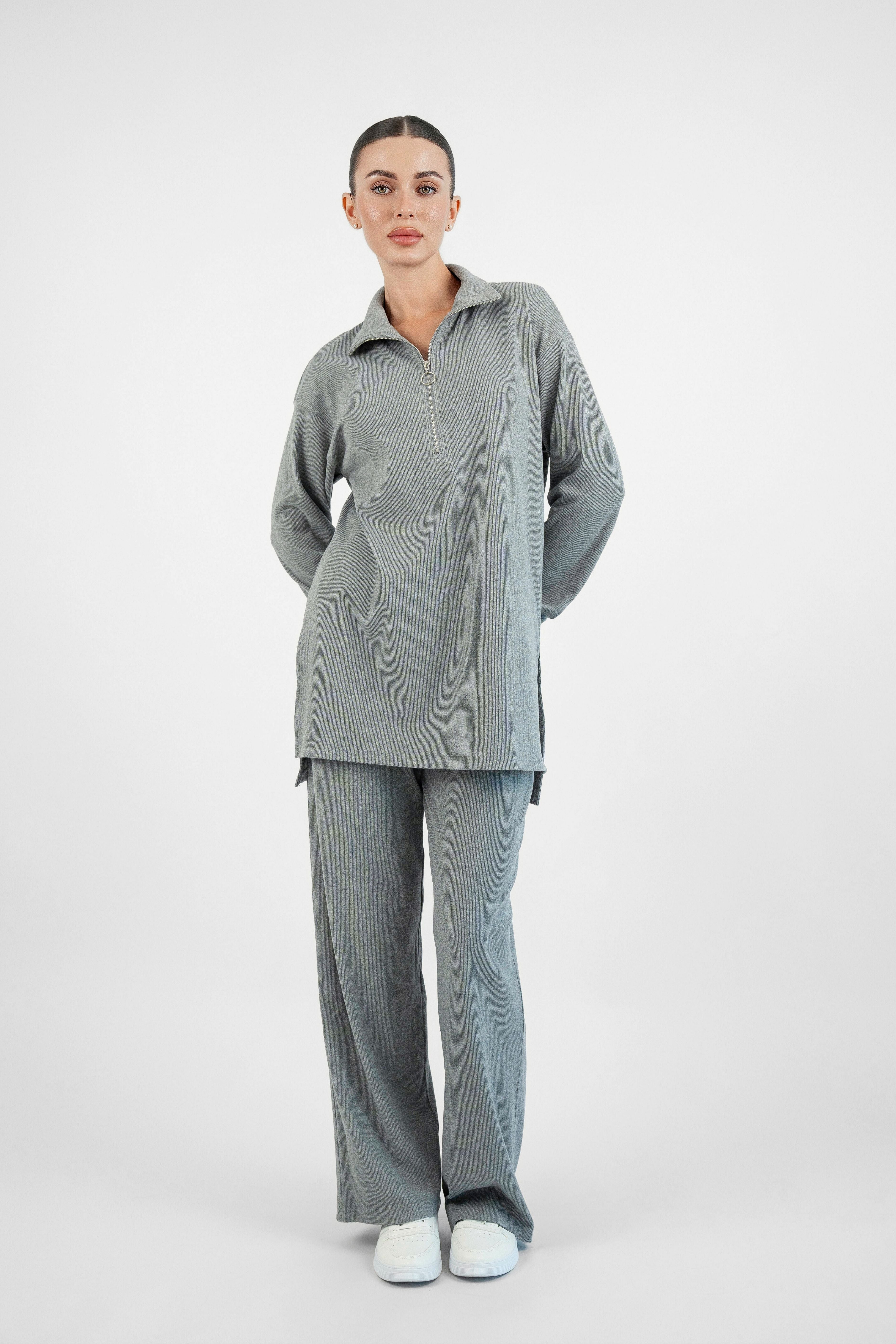 A girl is facing the camera in FARES' velour knit half zip with her hands behind her body. Colour description: Heather Grey.
