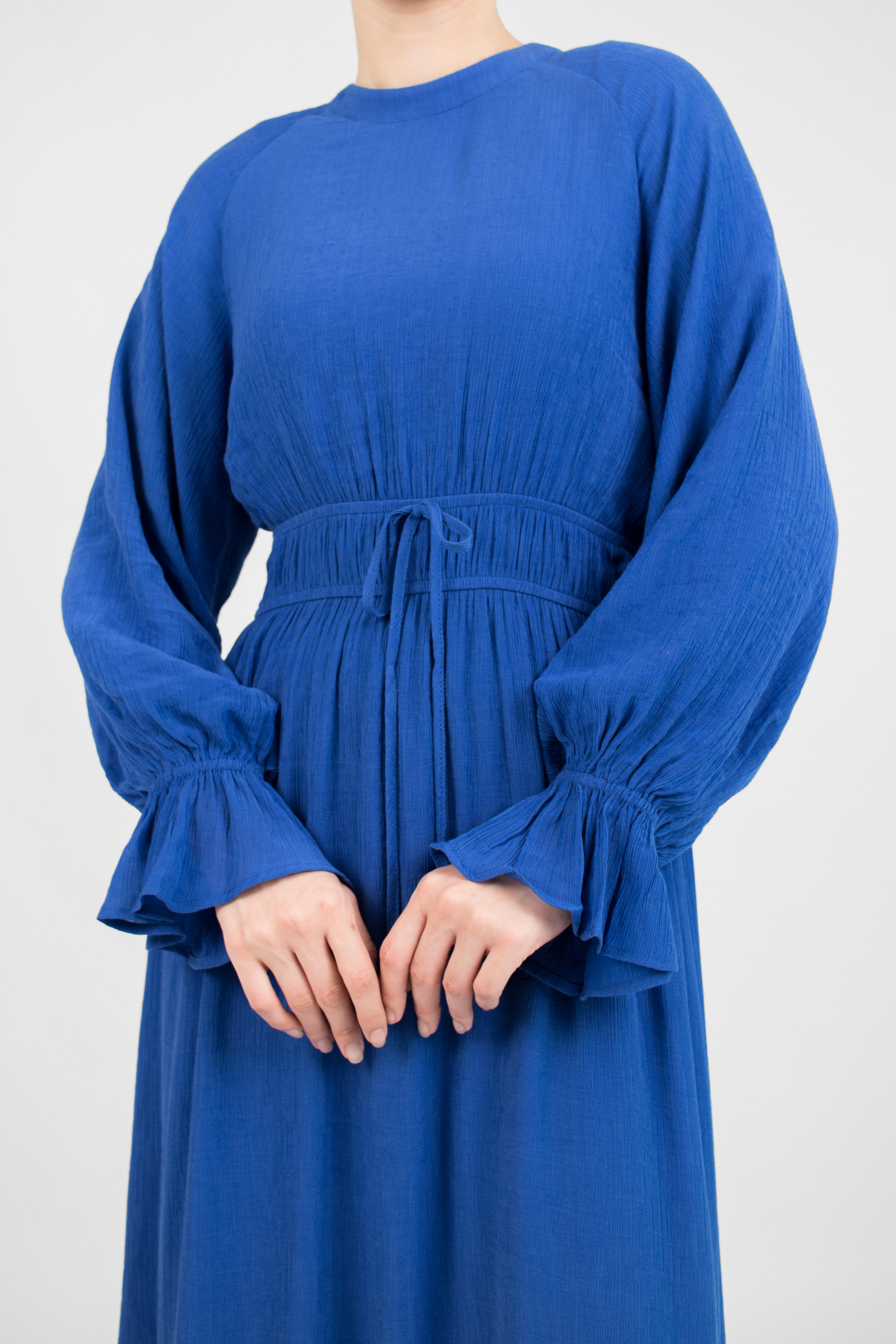 A closer look of a girl standing with her hands crossed front of her body in FARES' bow dress. Colour description: Sapphire