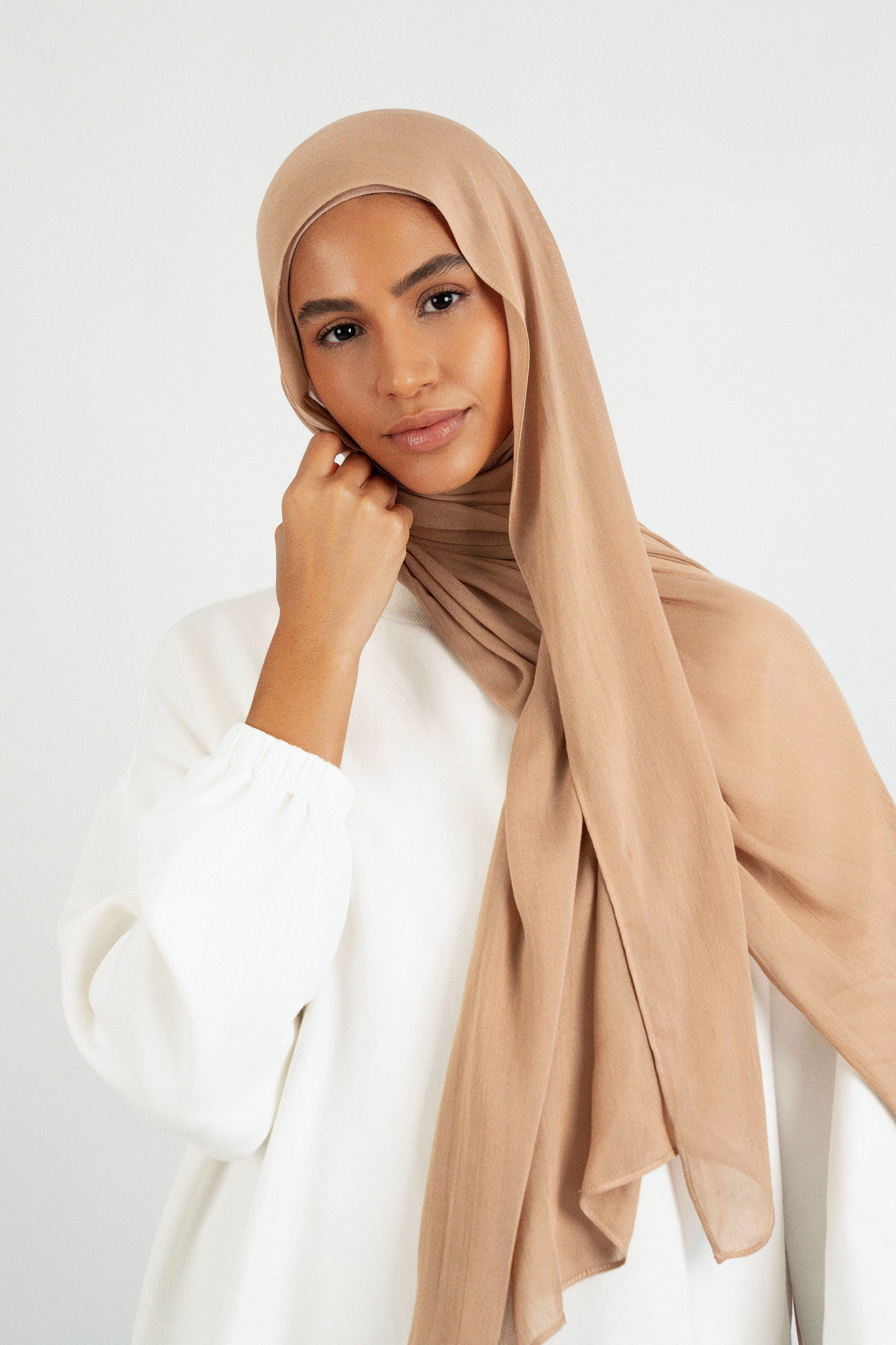 A model is wearing a Matching Butter Modal Hijab Set and touching her face. Colour: Almond